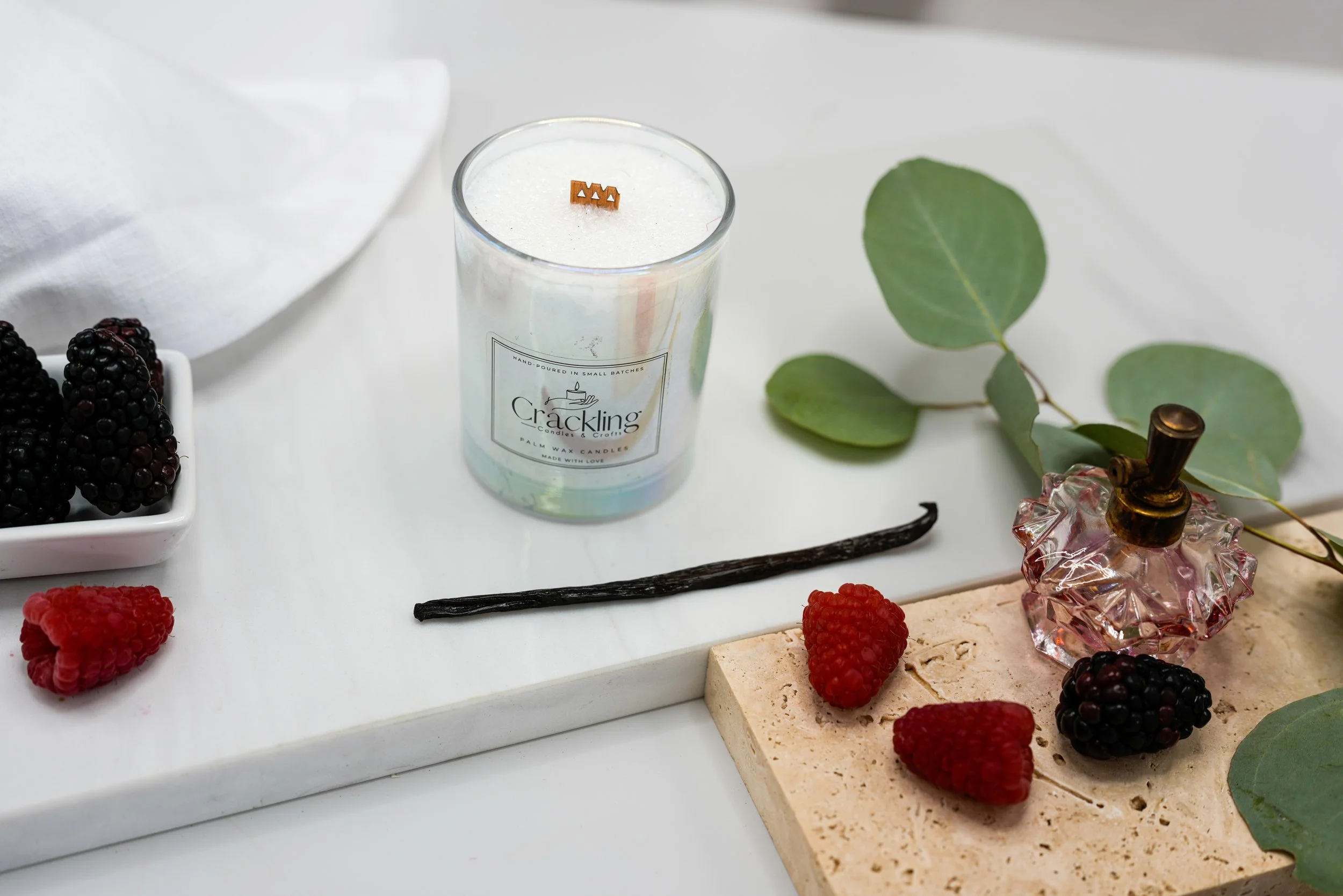 Top view of a Black Raspberry & Vanilla palm wax candle with a wooden wick, styled with raspberries, vanilla beans, and eucalyptus.