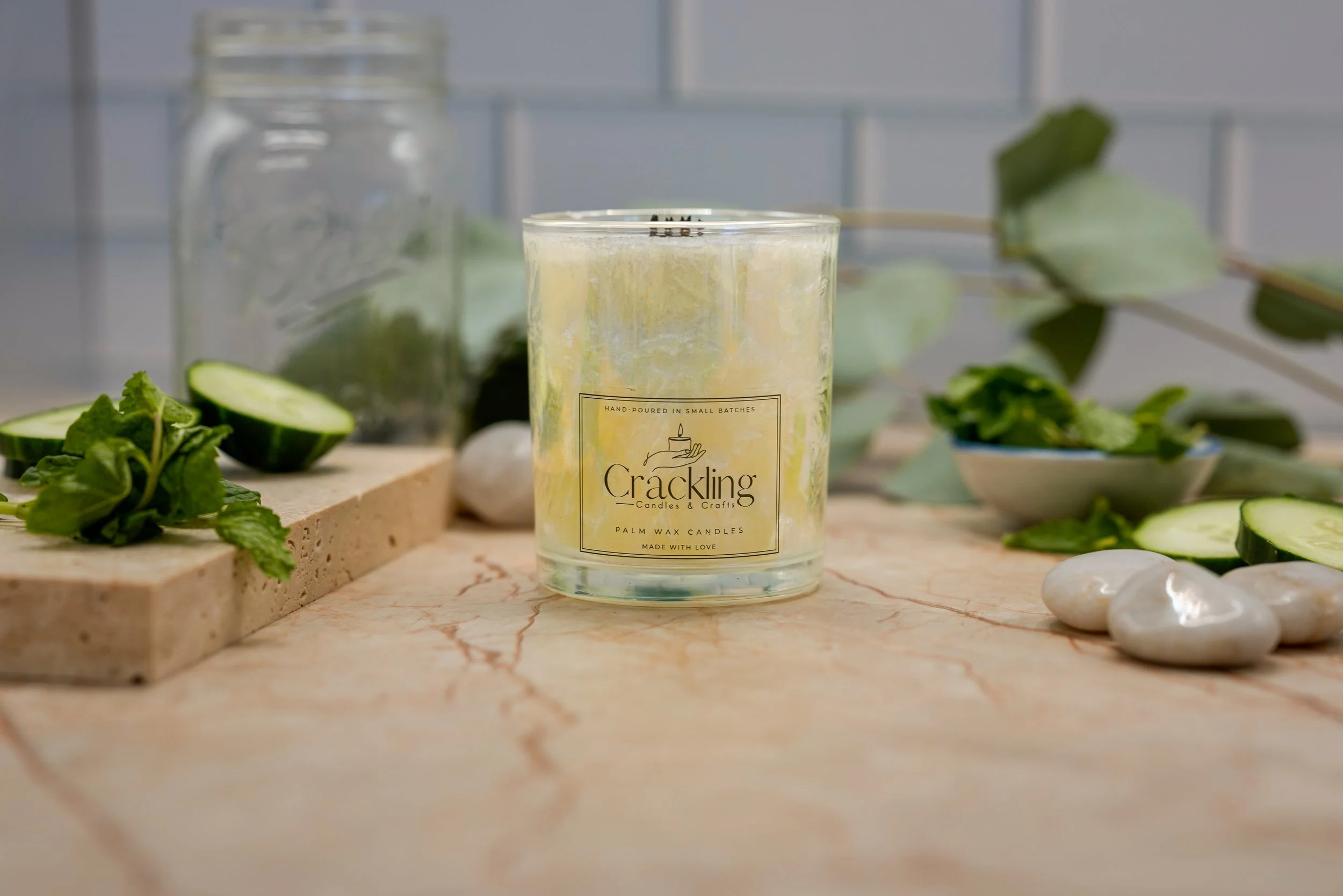 Front view of the Garden Mint & Cucumber candle in a glass jar, styled with cucumber slices and greenery against a gray tile background.