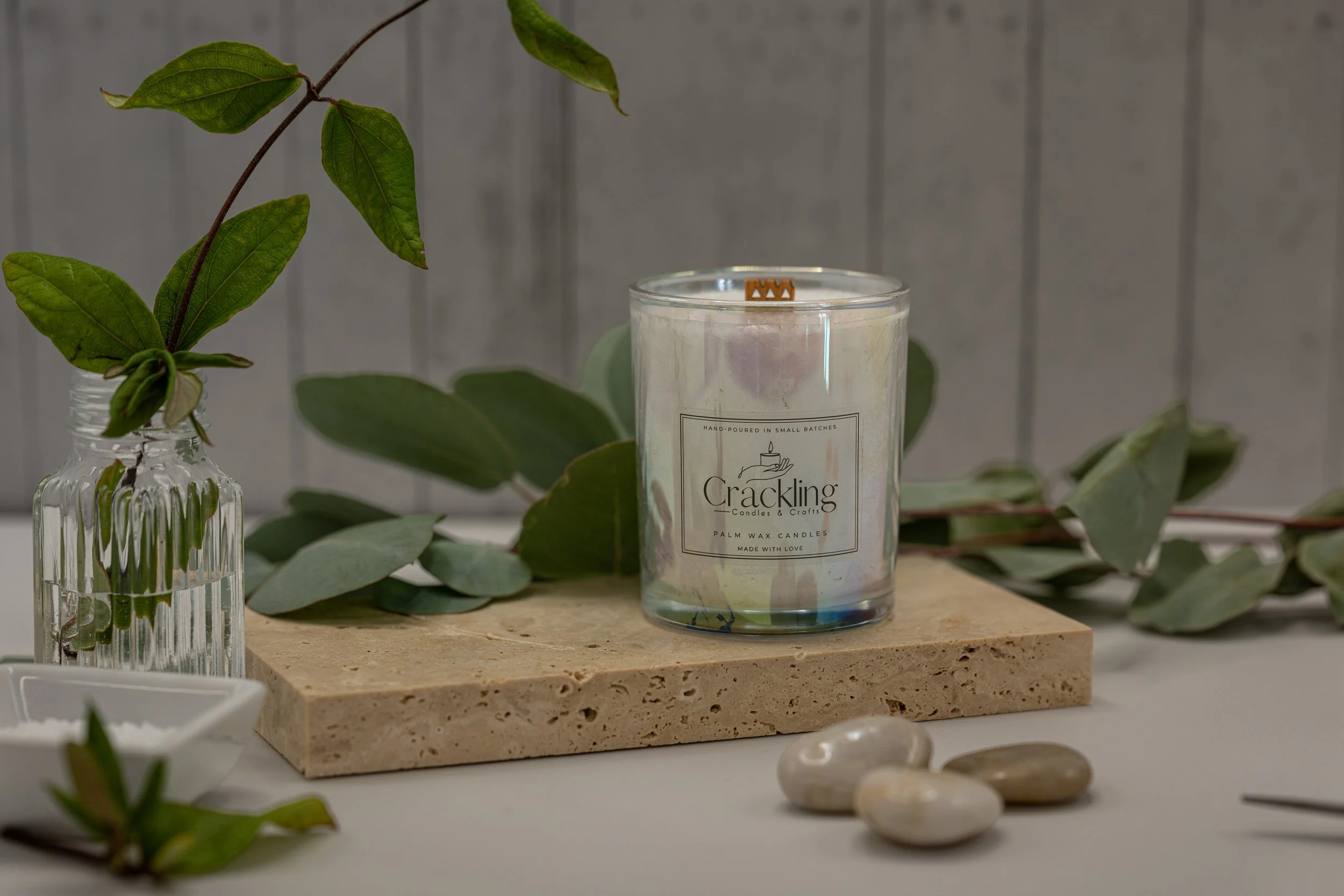 6 oz Dragon’s Blood palm wax candle in an iridescent glass holder on a light stone riser, styled with greenery and smooth stones