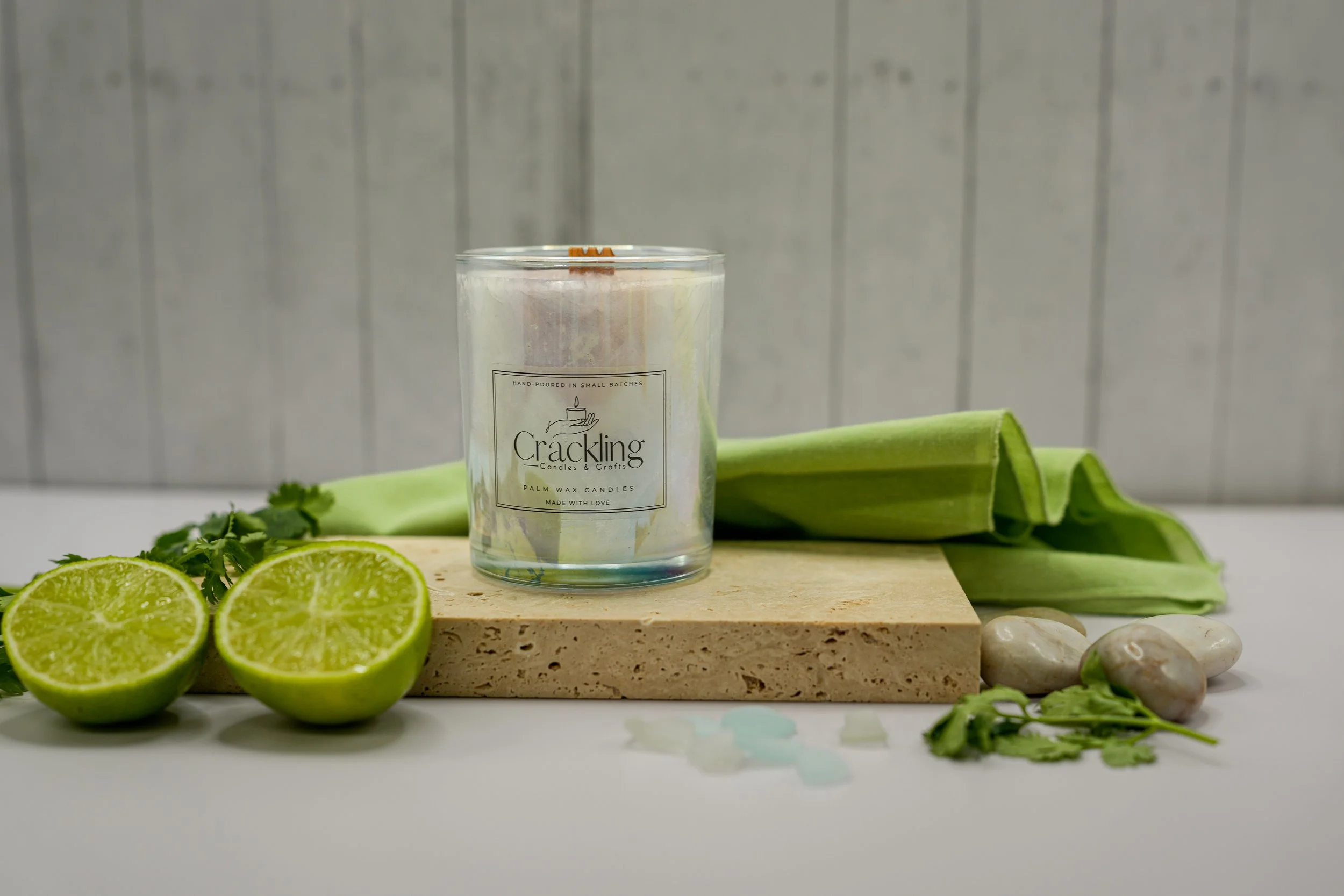 Lime Cilantro palm wax candle on a beige display slab with a lime half, cilantro sprigs, and folded green fabric.