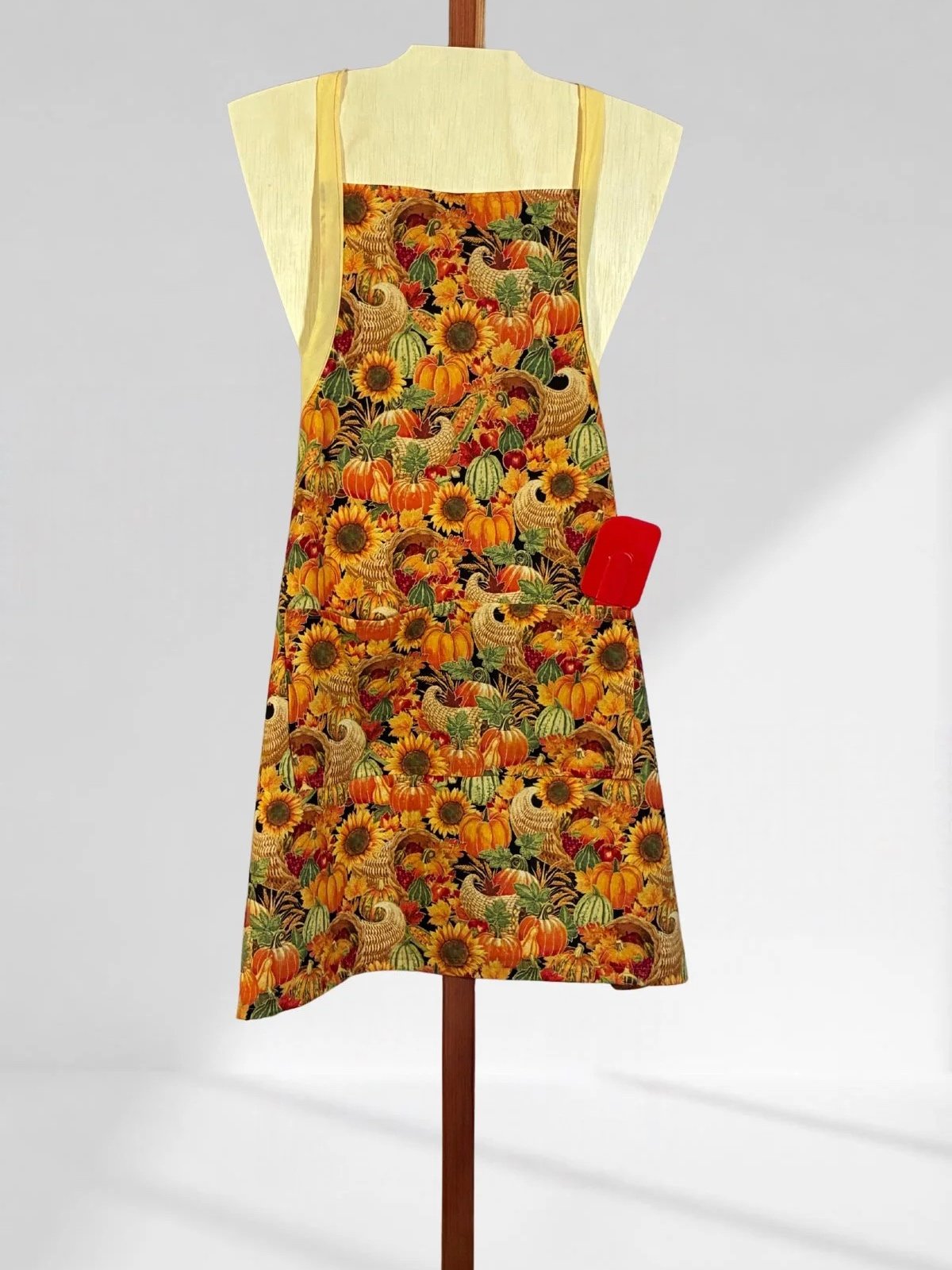 Close view of the adult harvest-print apron with a front pocket and a red spatula shown for display.