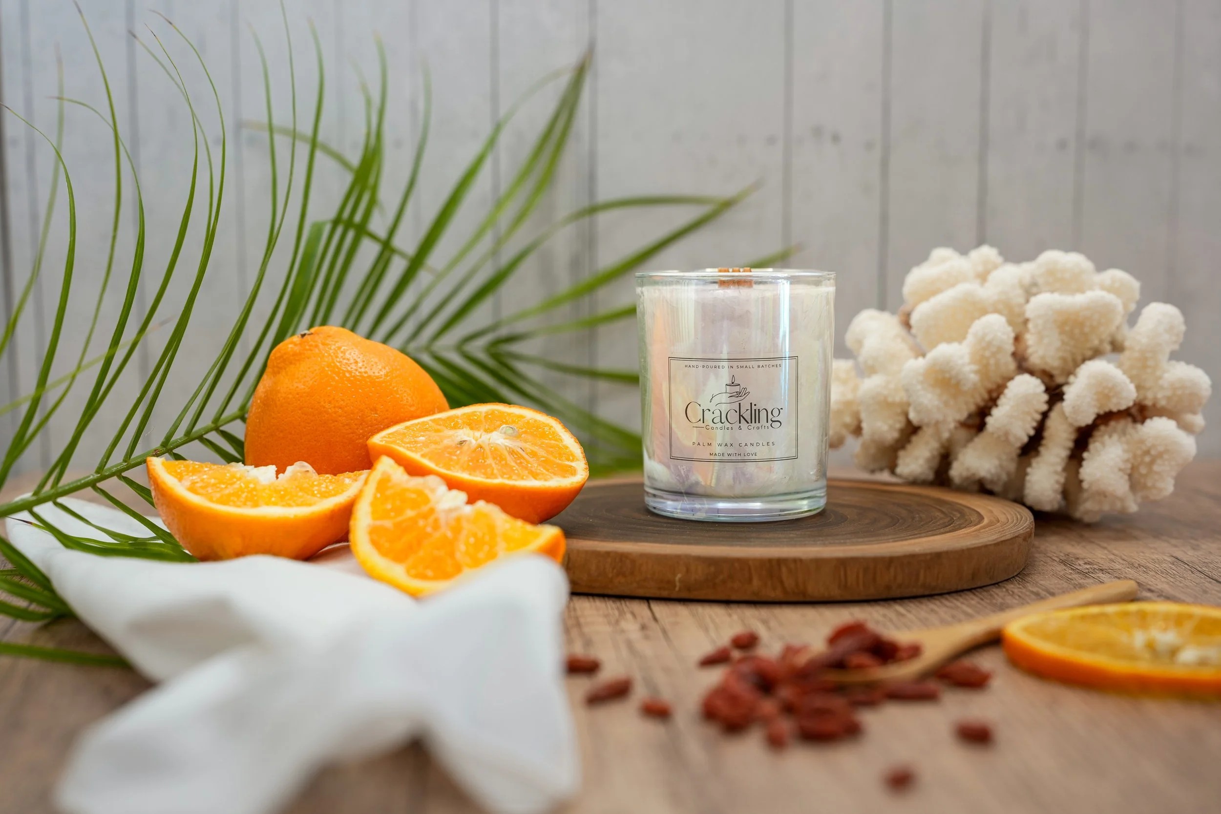 Bite Me candle displayed on a round wood riser with orange slices, tropical greenery, and warm natural accents.