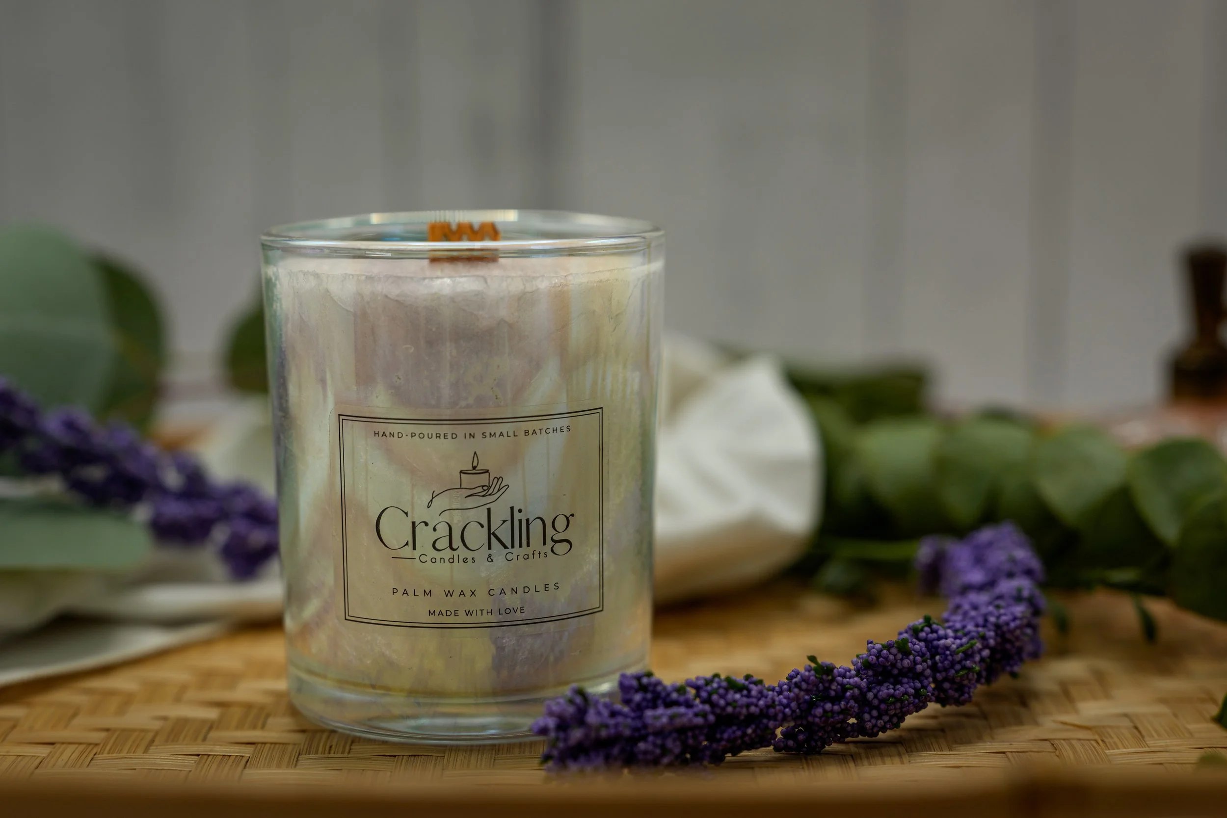 Palm wax candle in a clear glass jar, styled with purple flowers on a wooden surface.