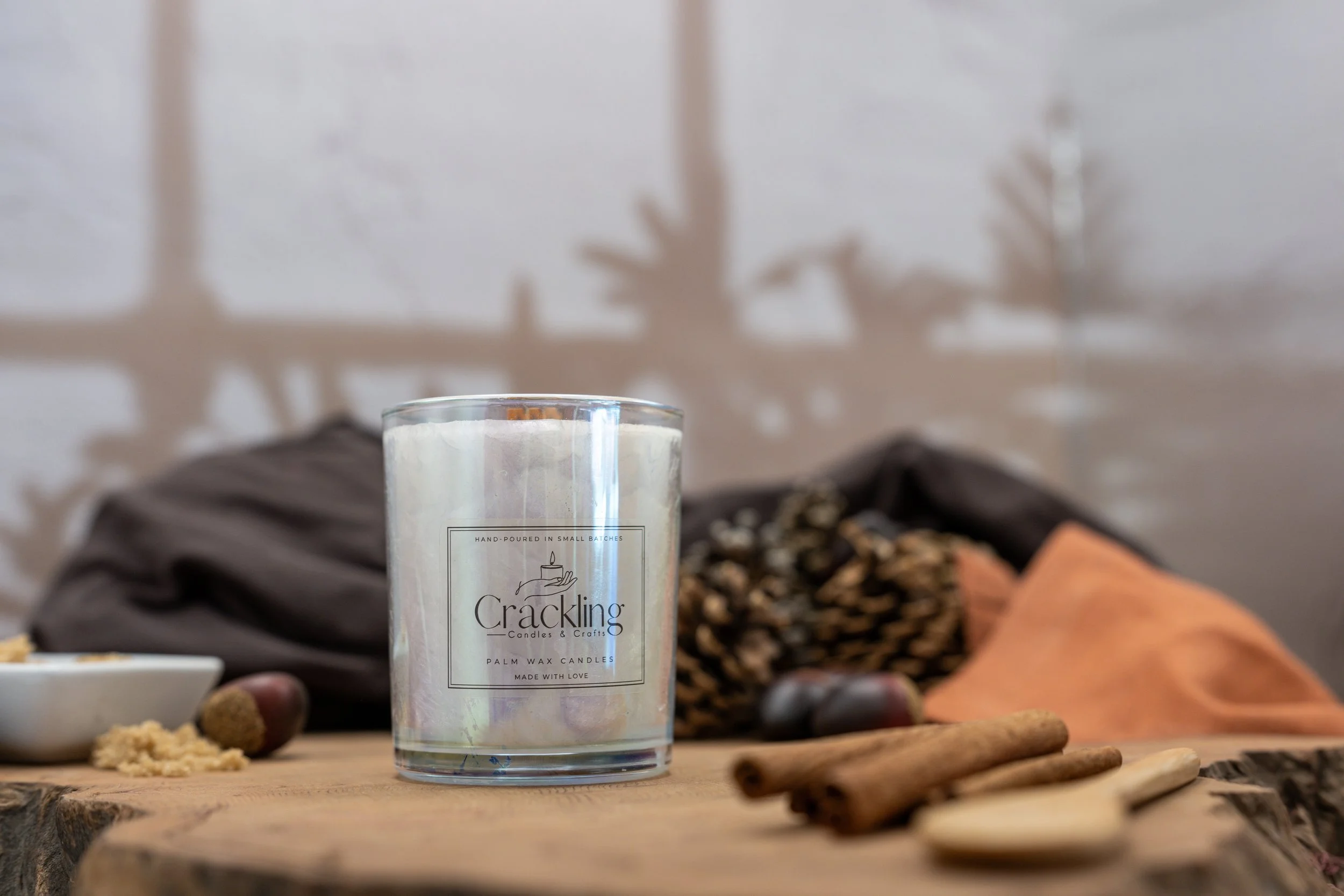 Palm wax candle in an iridescent glass jar on a wooden surface, styled with cinnamon sticks and dried botanicals.