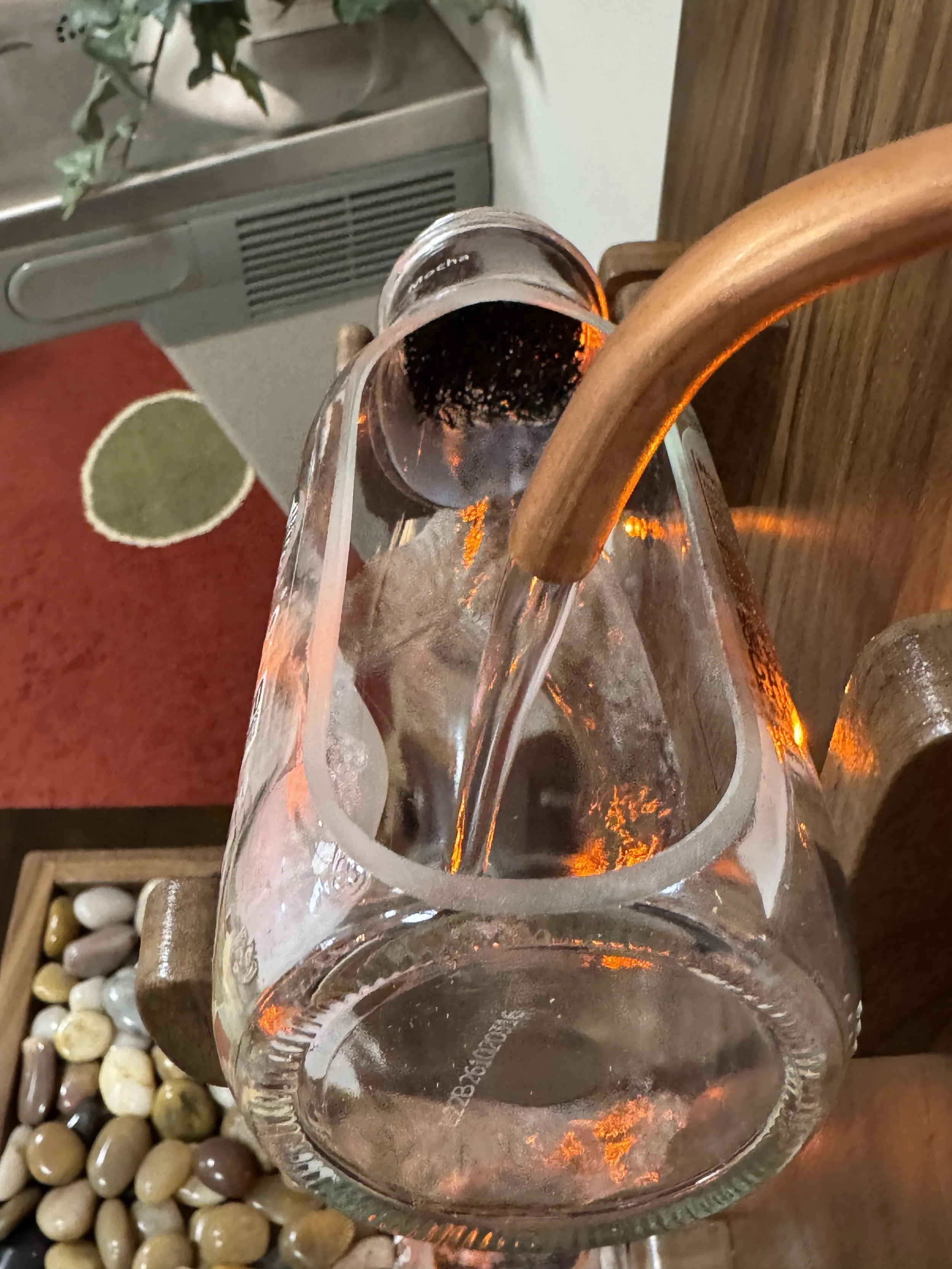 Close-up of a copper tube supplying water to a glass bottle on the black walnut fountain.