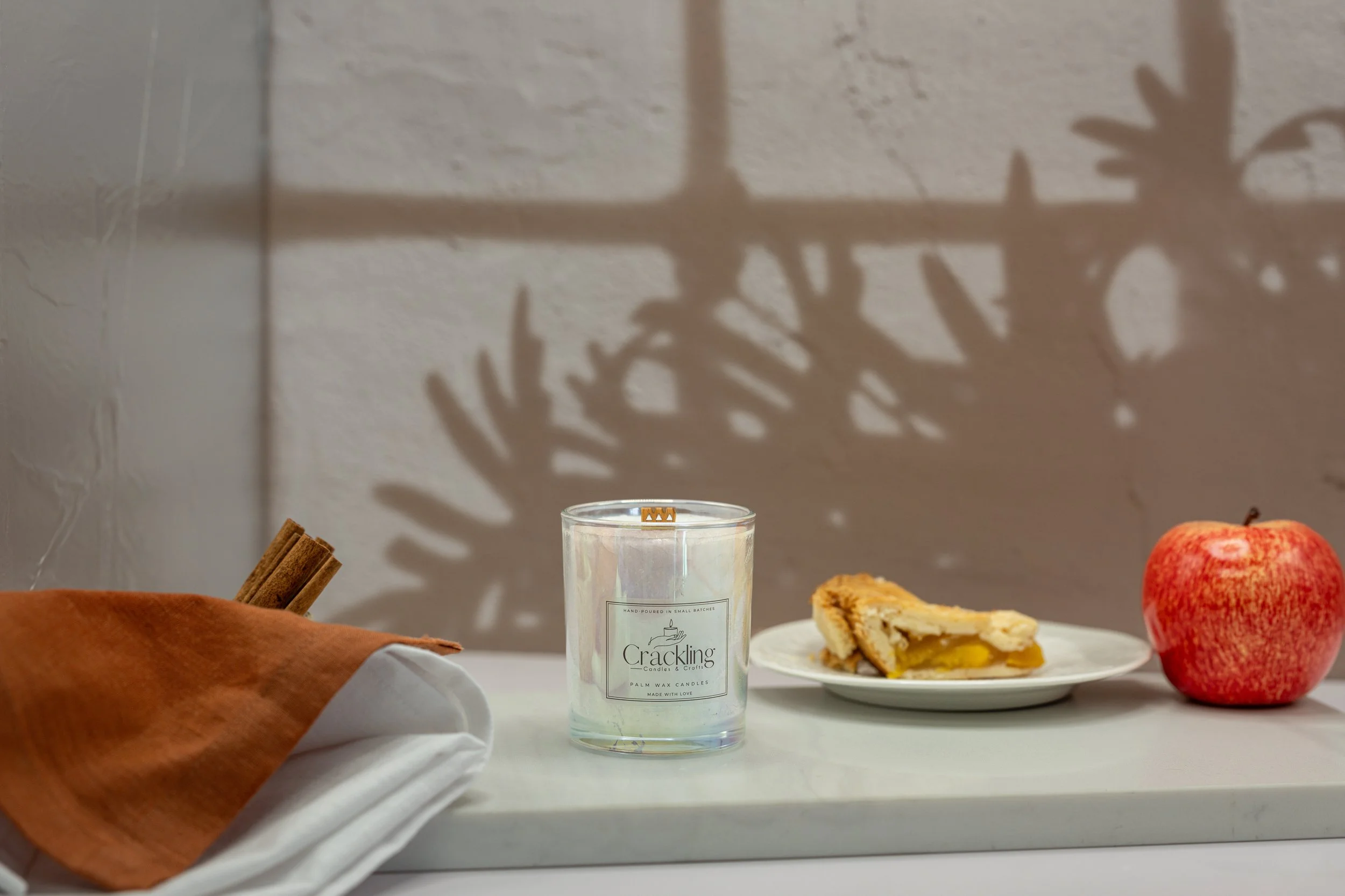 6 oz Hot Baked Apple Pie palm wax candle styled beside a slice of apple pie and cinnamon sticks