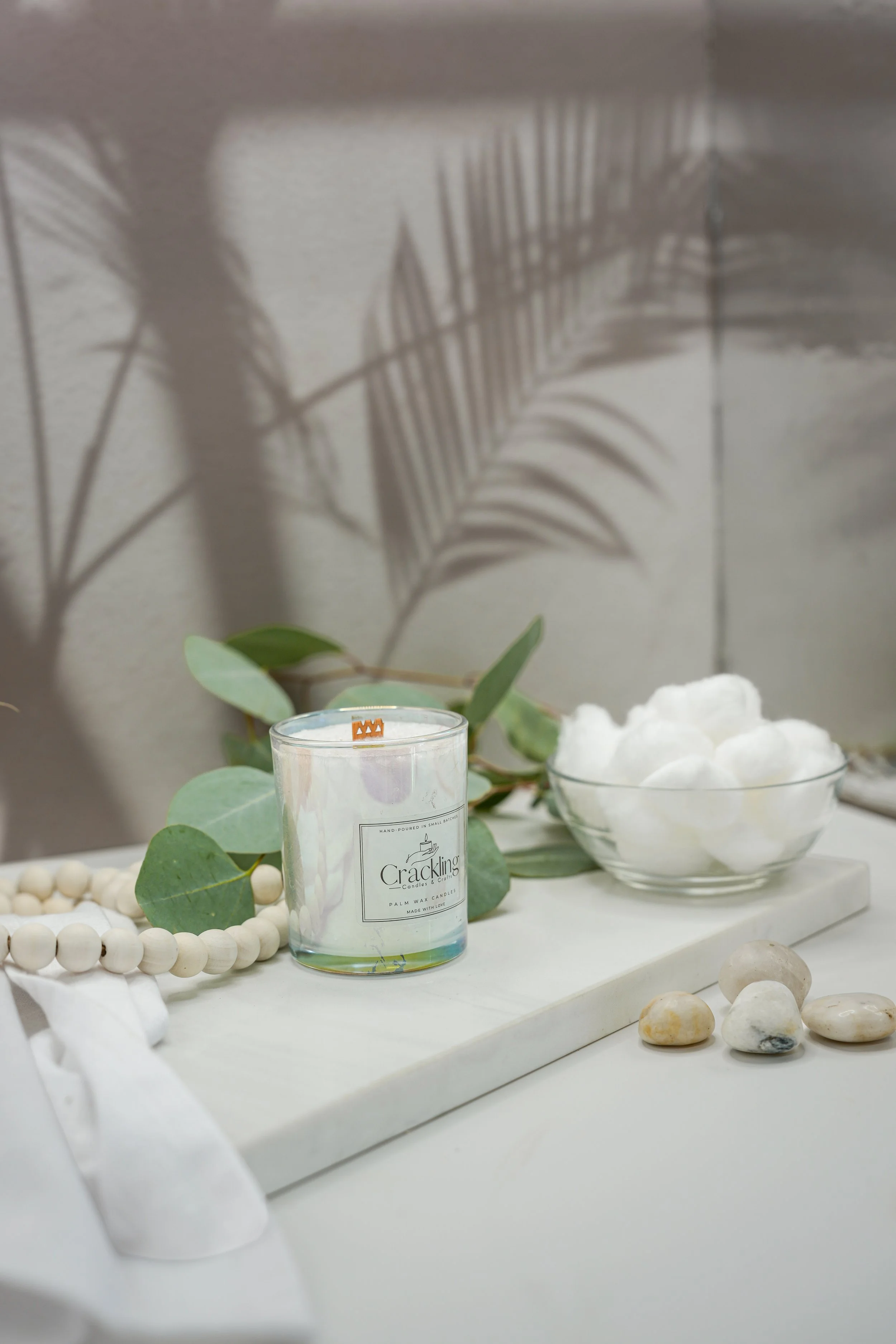 6 oz Baby Powder candle styled with eucalyptus, white cotton, smooth stones, and natural wooden beads.