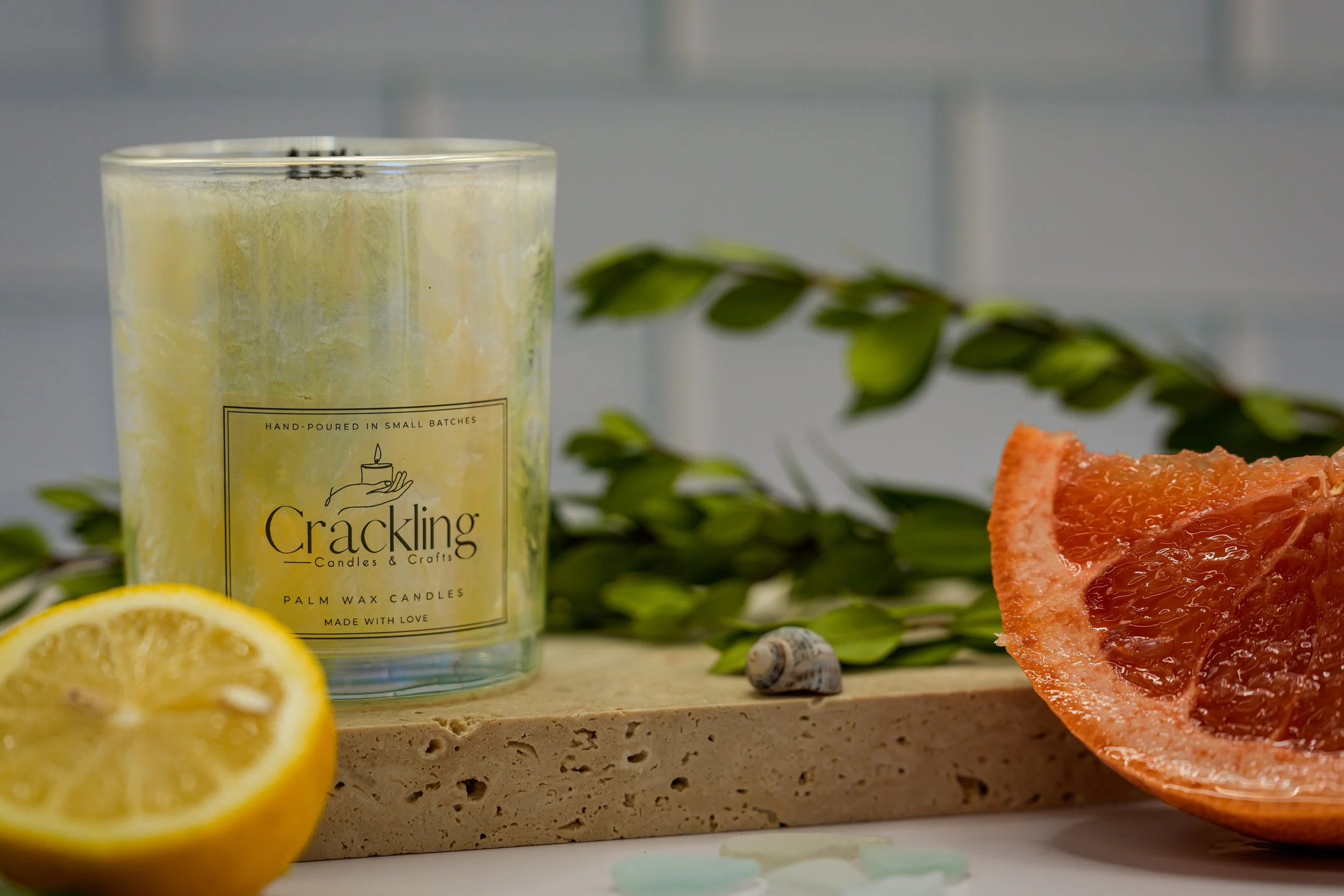 Sage & Citrus candle on a stone riser with a lemon half, grapefruit, and green leaves.