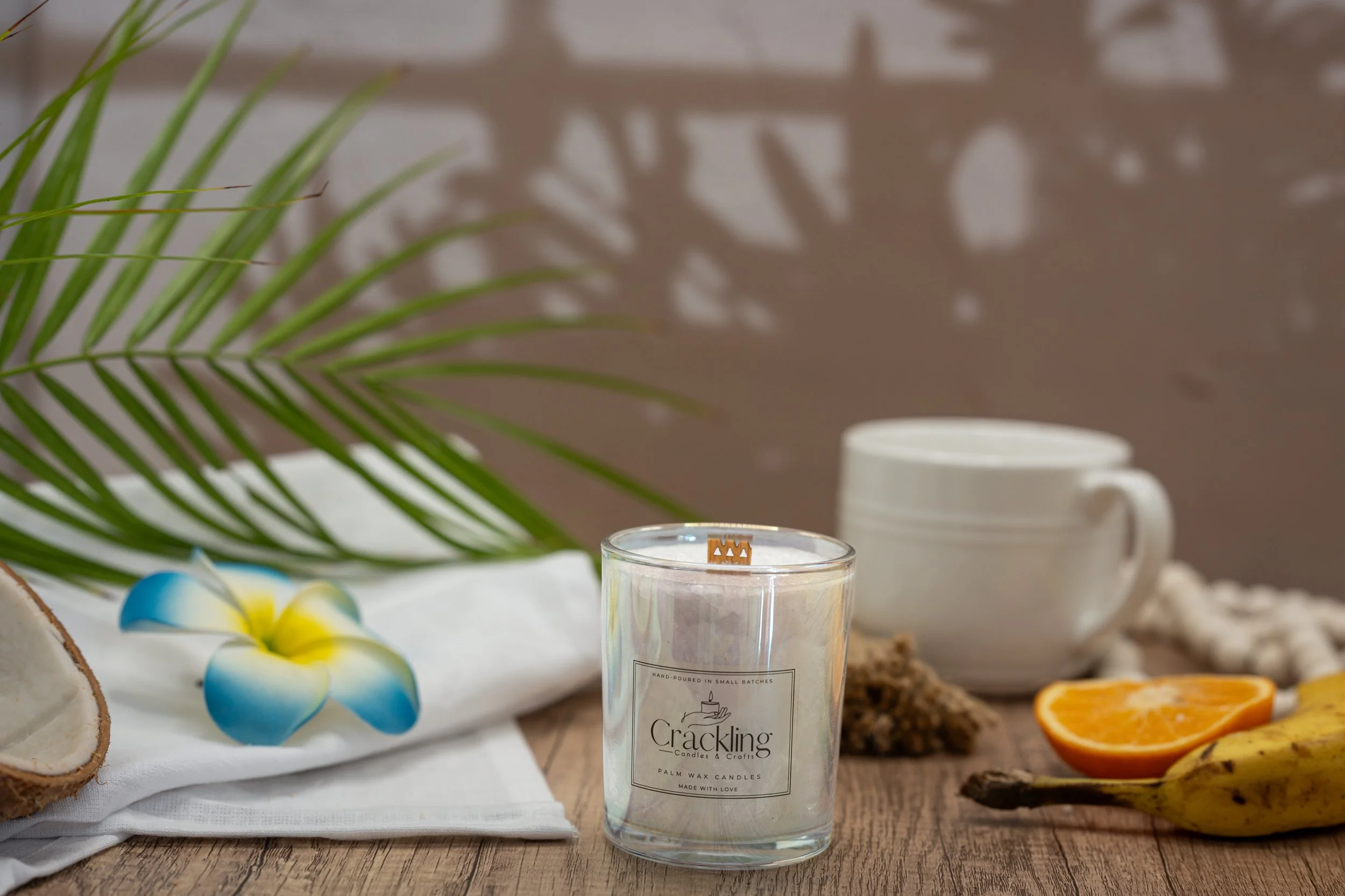 Café de Olla candle displayed with a white coffee mug, cinnamon, citrus, and tropical greenery in a warm coffee-inspired setting.