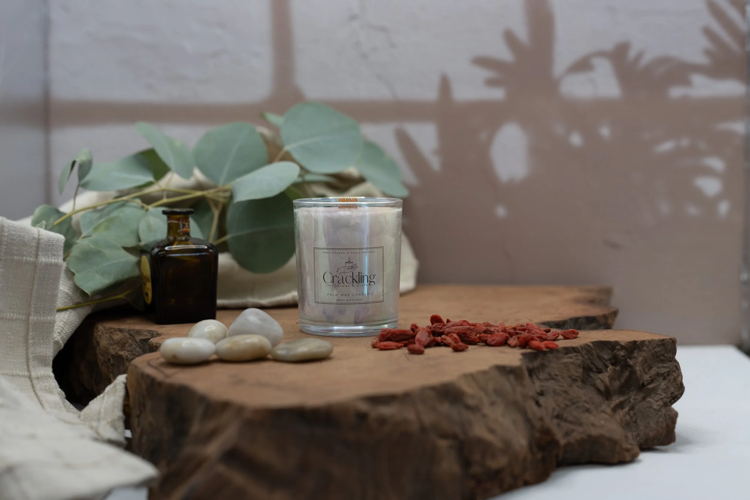 Wide view of a 6 oz Tobacco & Oud candle styled with eucalyptus, smooth stones, and an amber bottle on a wood slab