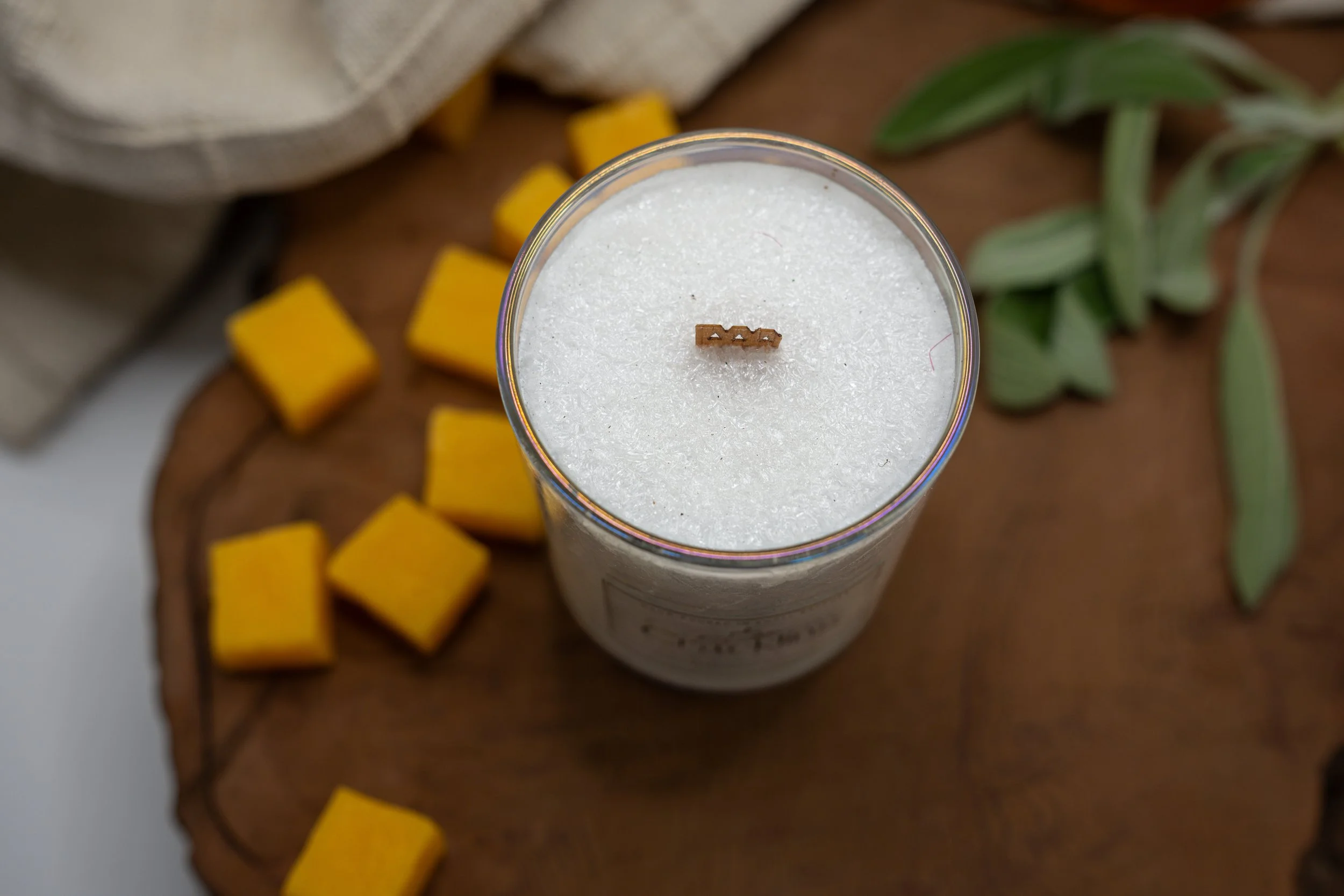 Top view of a palm wax candle with a centered wooden wick, surrounded by mango cubes and sage leaves.