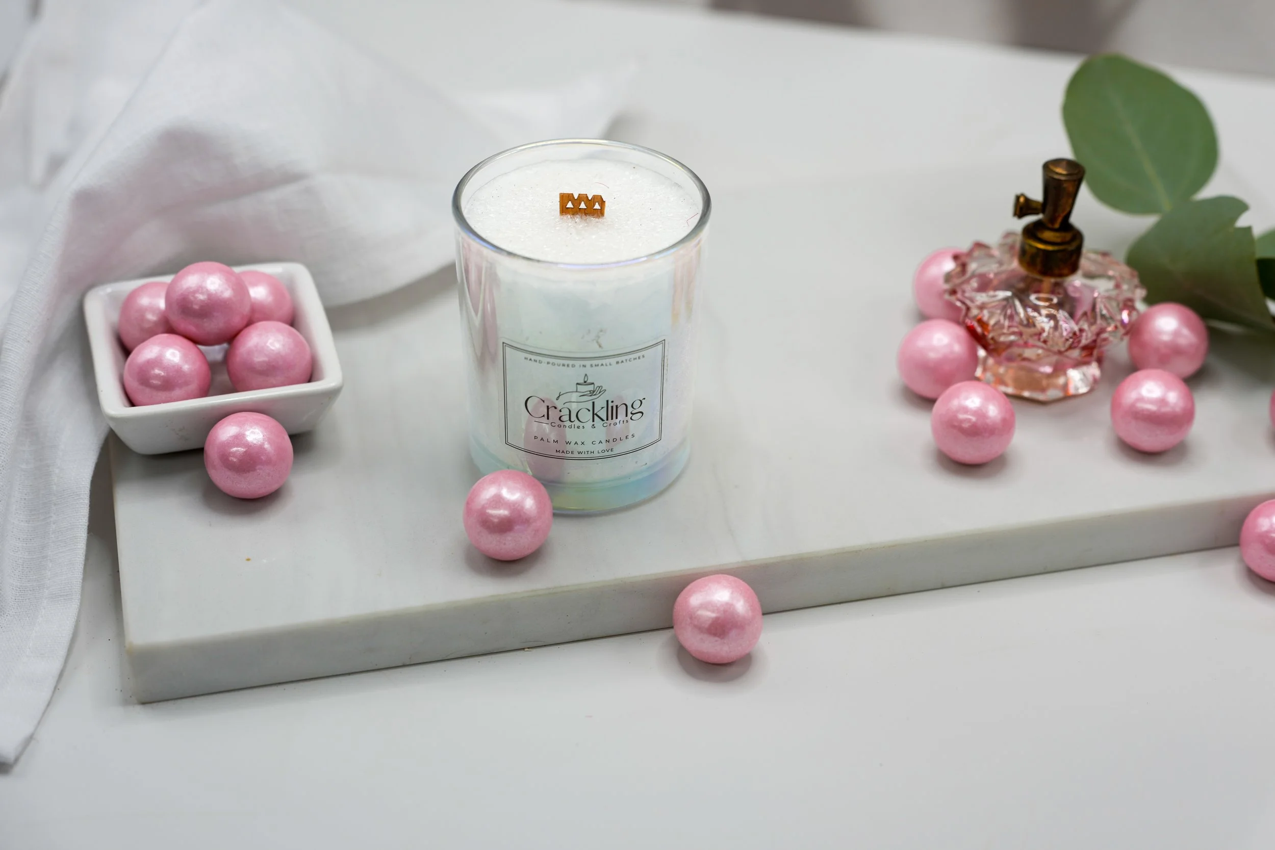 Close-up of a handcrafted Bubble Gum candle with a wooden wick, styled with shiny pink gumballs in a bright neutral setting.