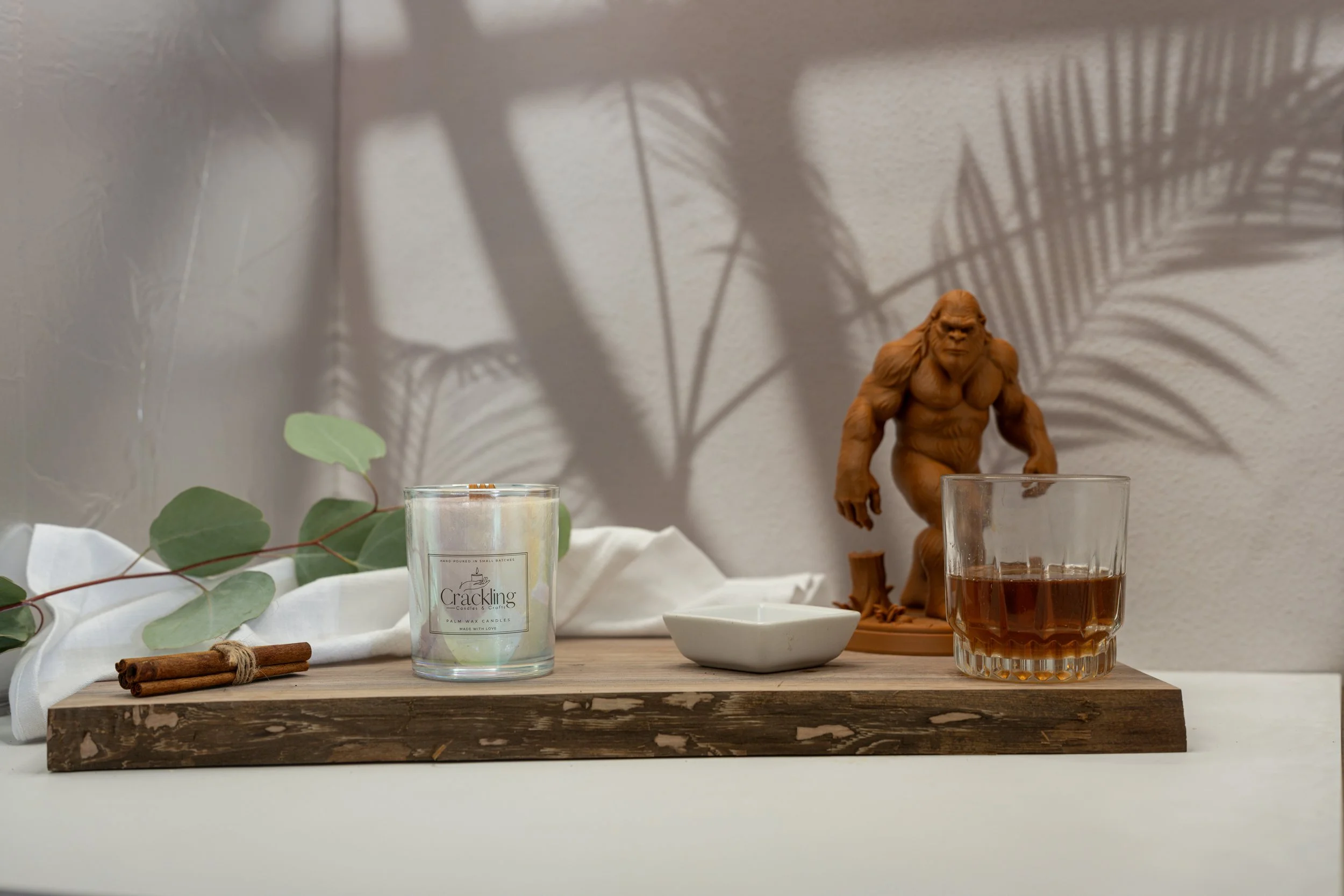 6 oz Coffee & Whiskey palm wax candle styled with a whiskey glass, Bigfoot figure, eucalyptus, and warm rustic decor.
