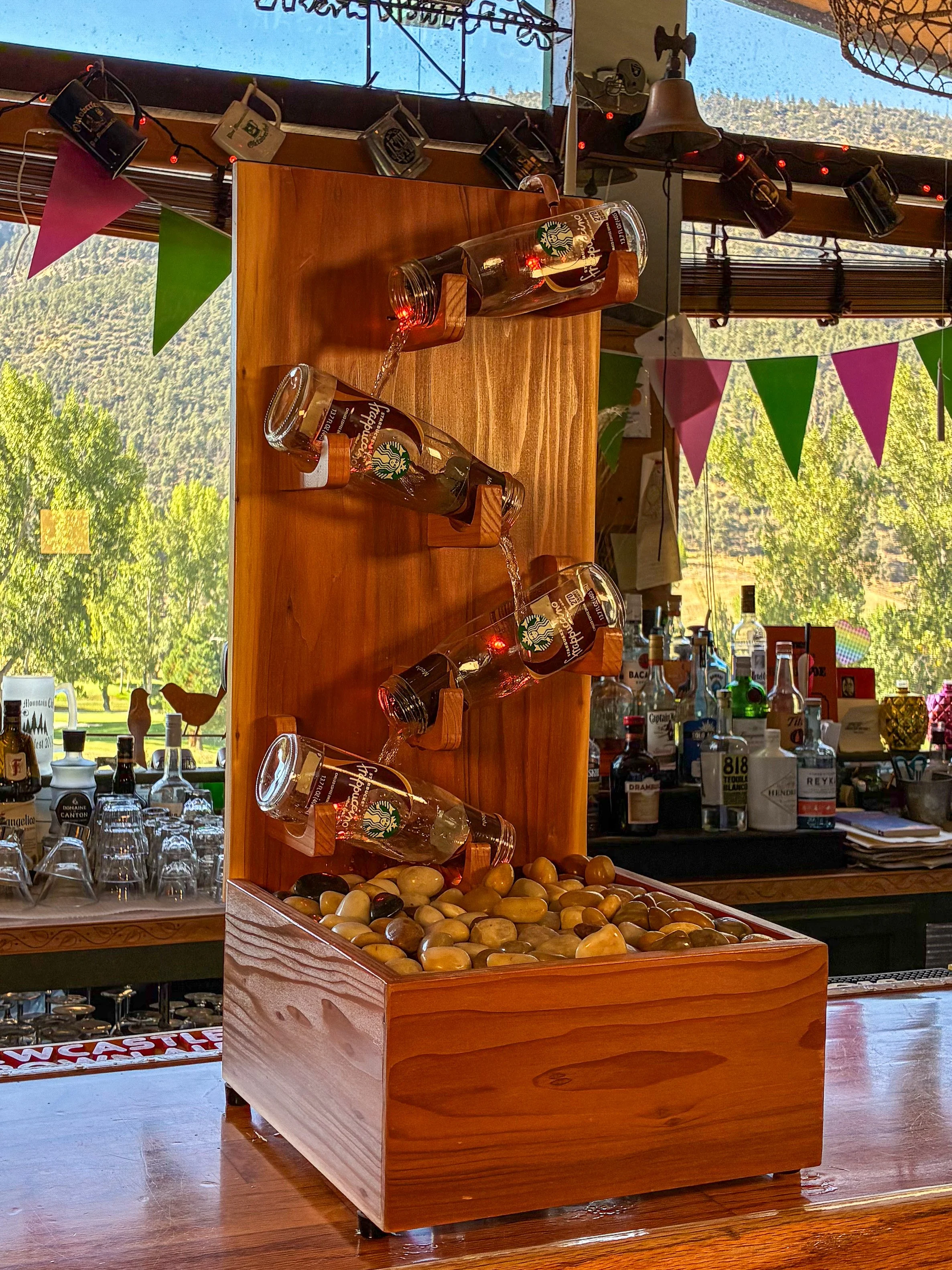 Angled view of four Starbucks Frappuccino bottles arranged above a river rock basin in a handcrafted redwood fountain.