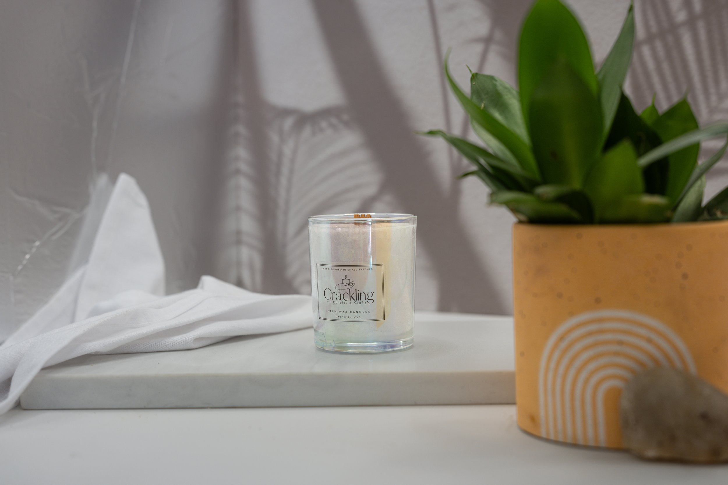 6 oz Agave palm wax candle styled with soft white linen and a green plant in a warm patterned pot.