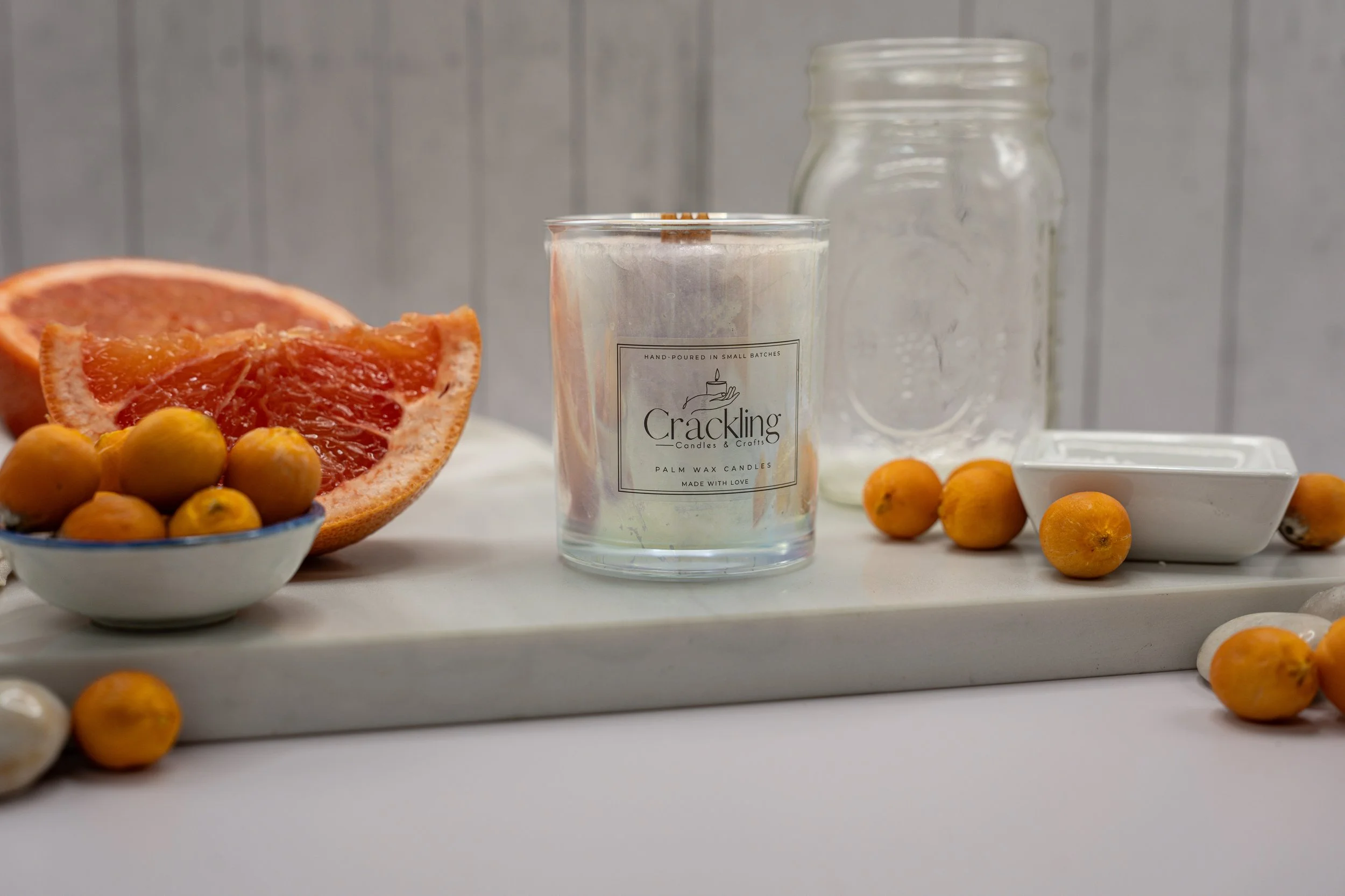 Grapefruit & Kumquat candle on a light display surface with grapefruit and kumquats nearby.