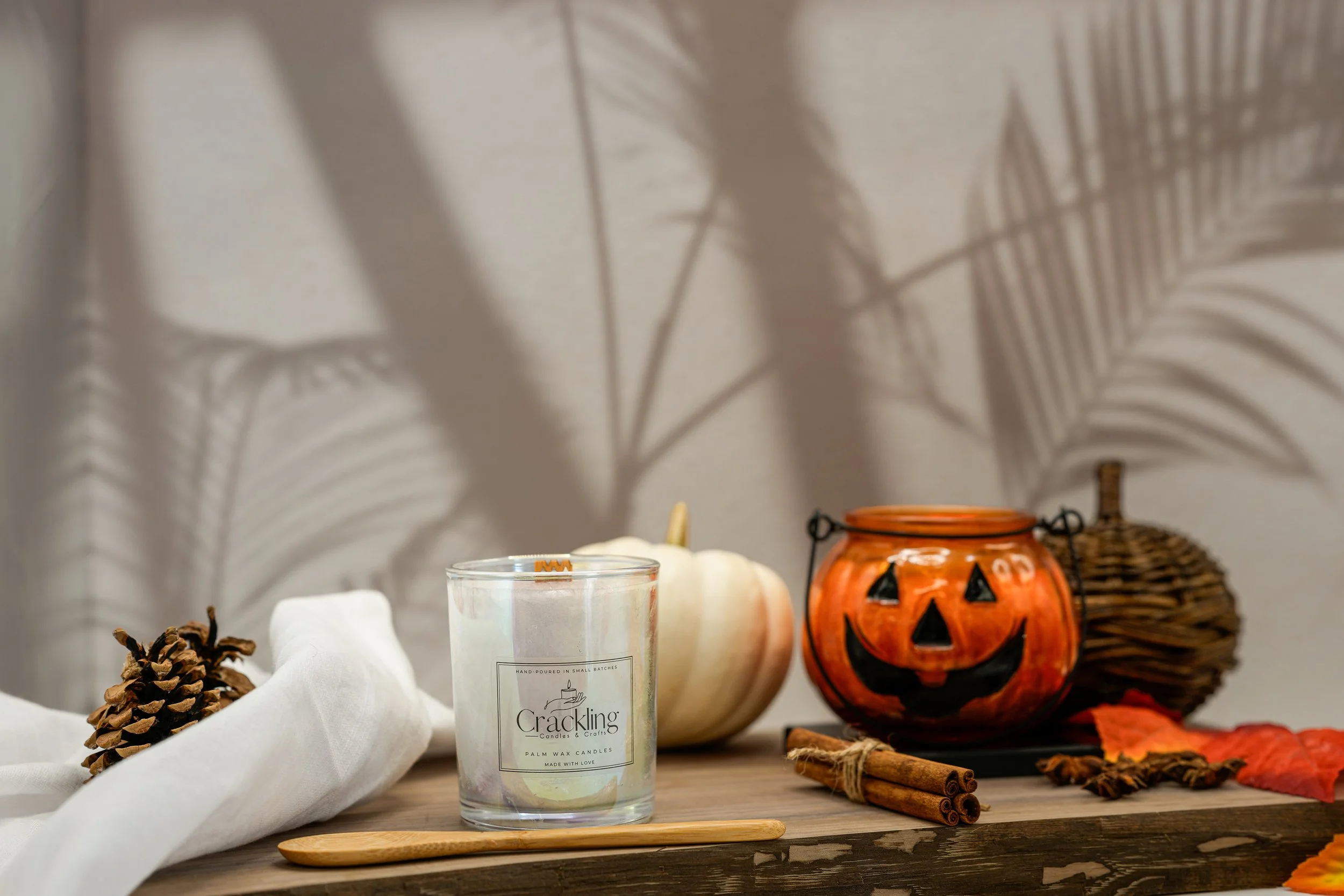 12 oz Pumpkin Spice Glass Pumpkin Candle glowing in a warm fall display with white pumpkins and rustic seasonal decor.