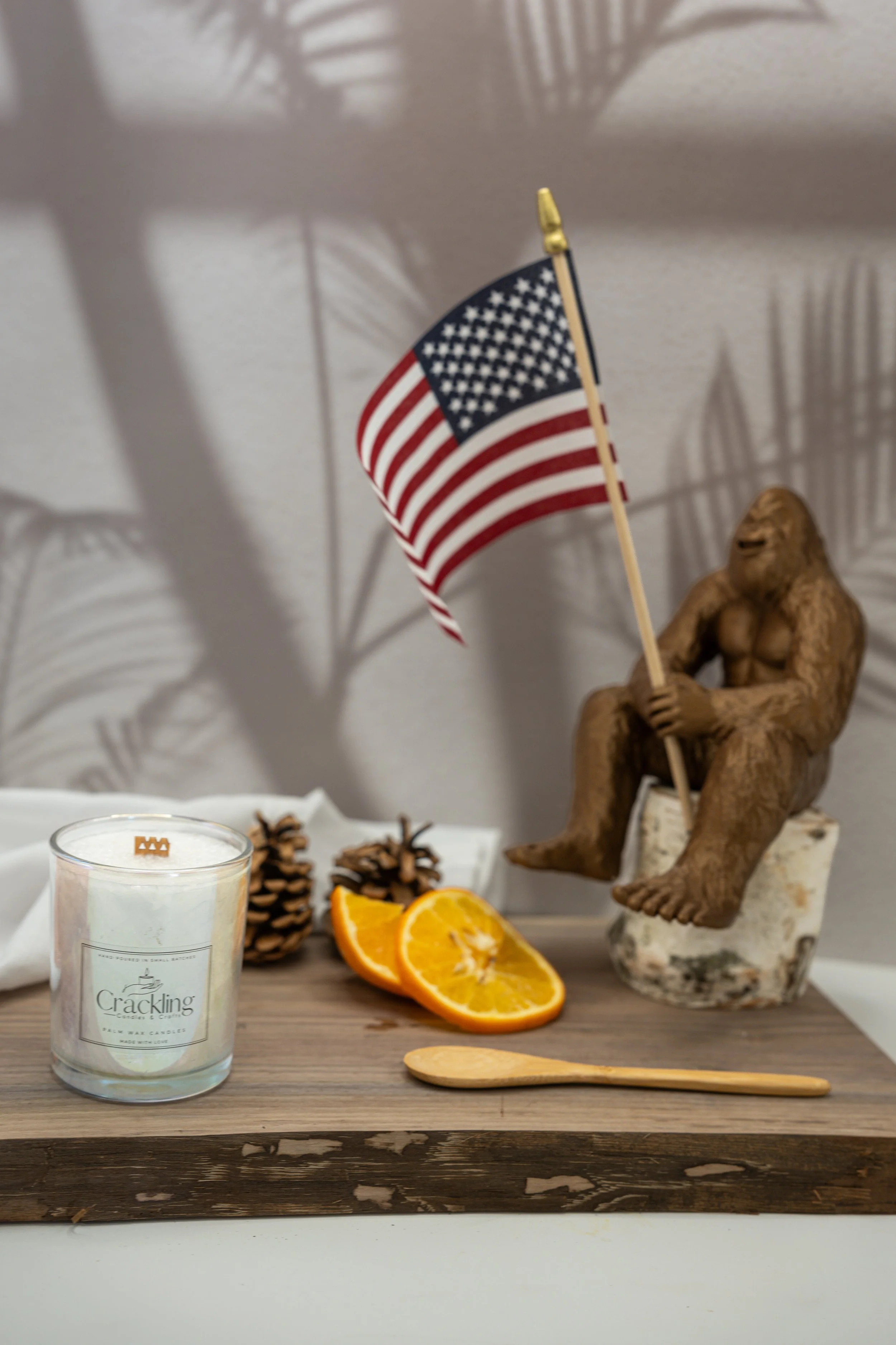 6 oz Cinnamon scented palm wax candle with a wooden wick, styled with Bigfoot, an American flag, orange slices, and cinnamon sticks.