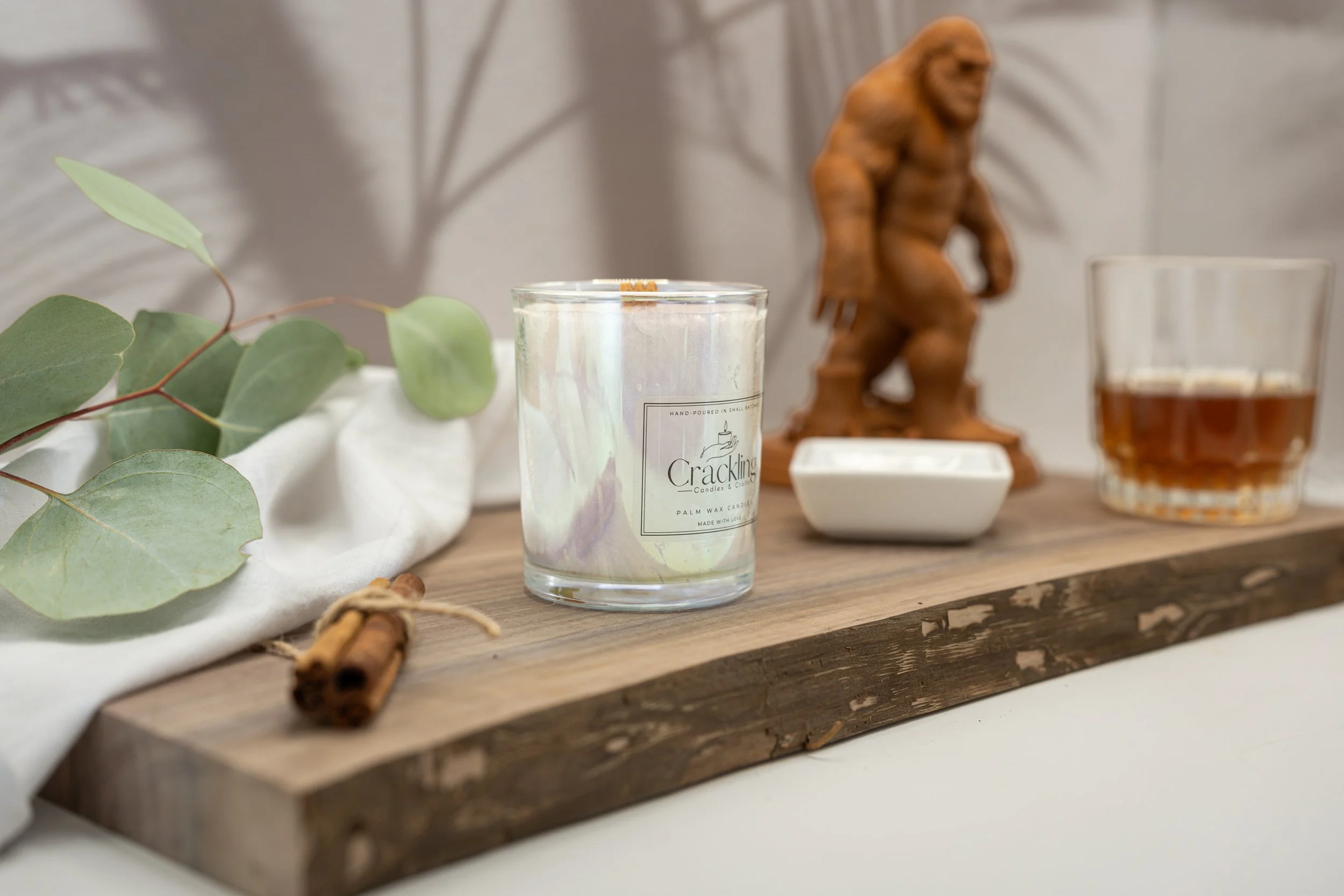 Hand-poured Coffee & Whiskey candle with a wooden wick, displayed with a Bigfoot figure and natural rustic accents.