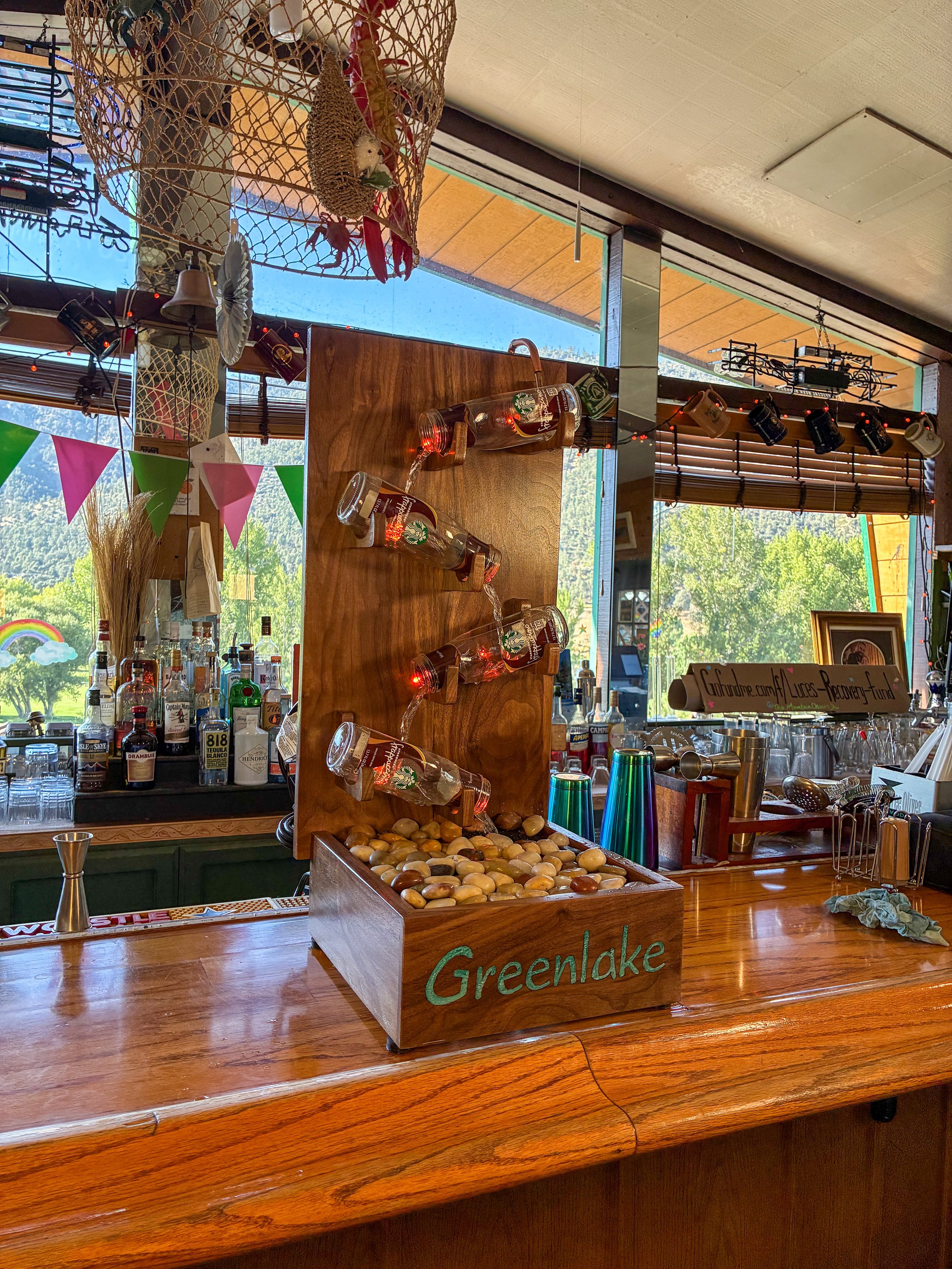 Black walnut Frappuccino bottle fountain displayed on a wooden bar counter with windows behind it.