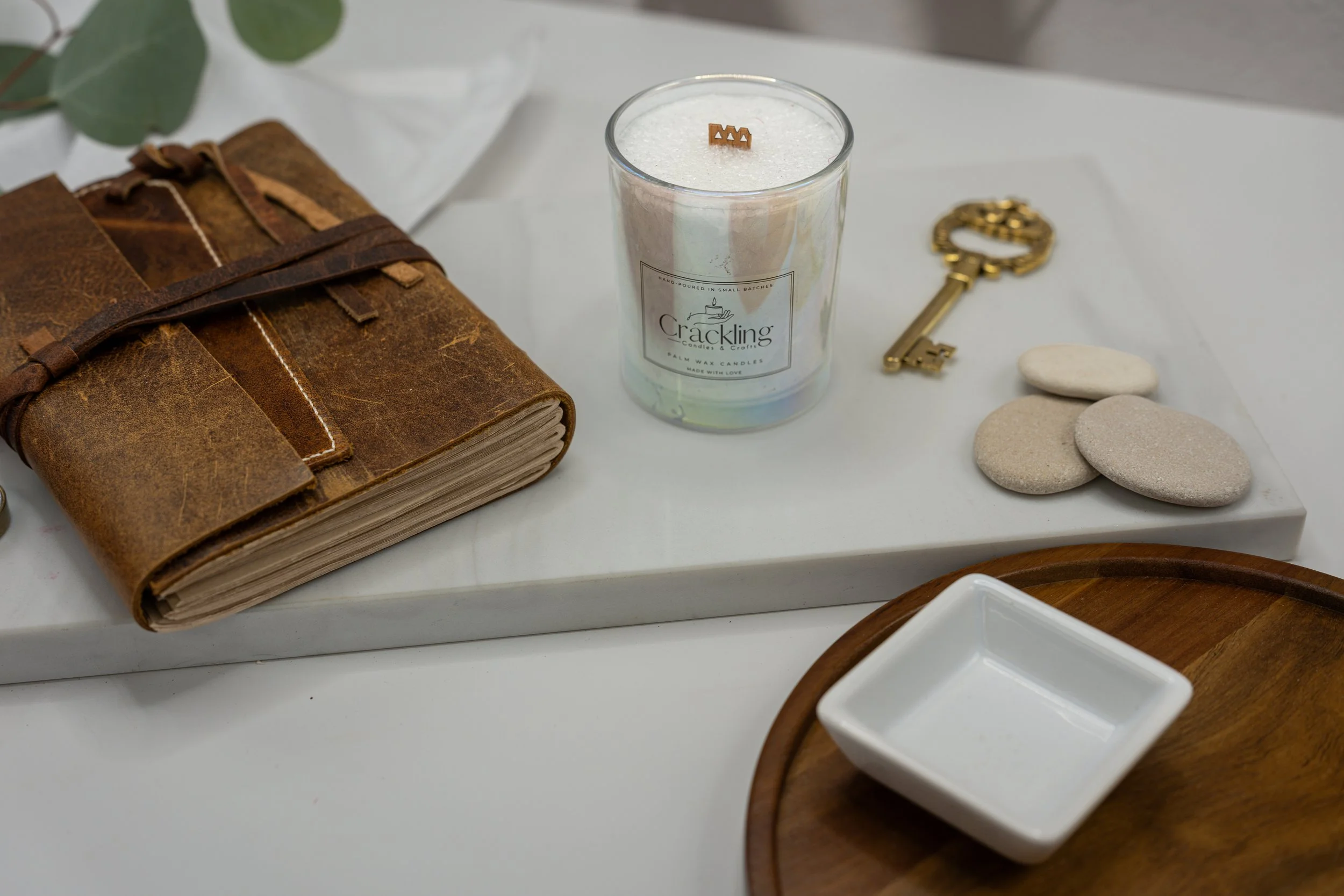 Bergamot and Mandarin candle displayed beside a leather journal, antique brass key, smooth stones, and soft white linen.
