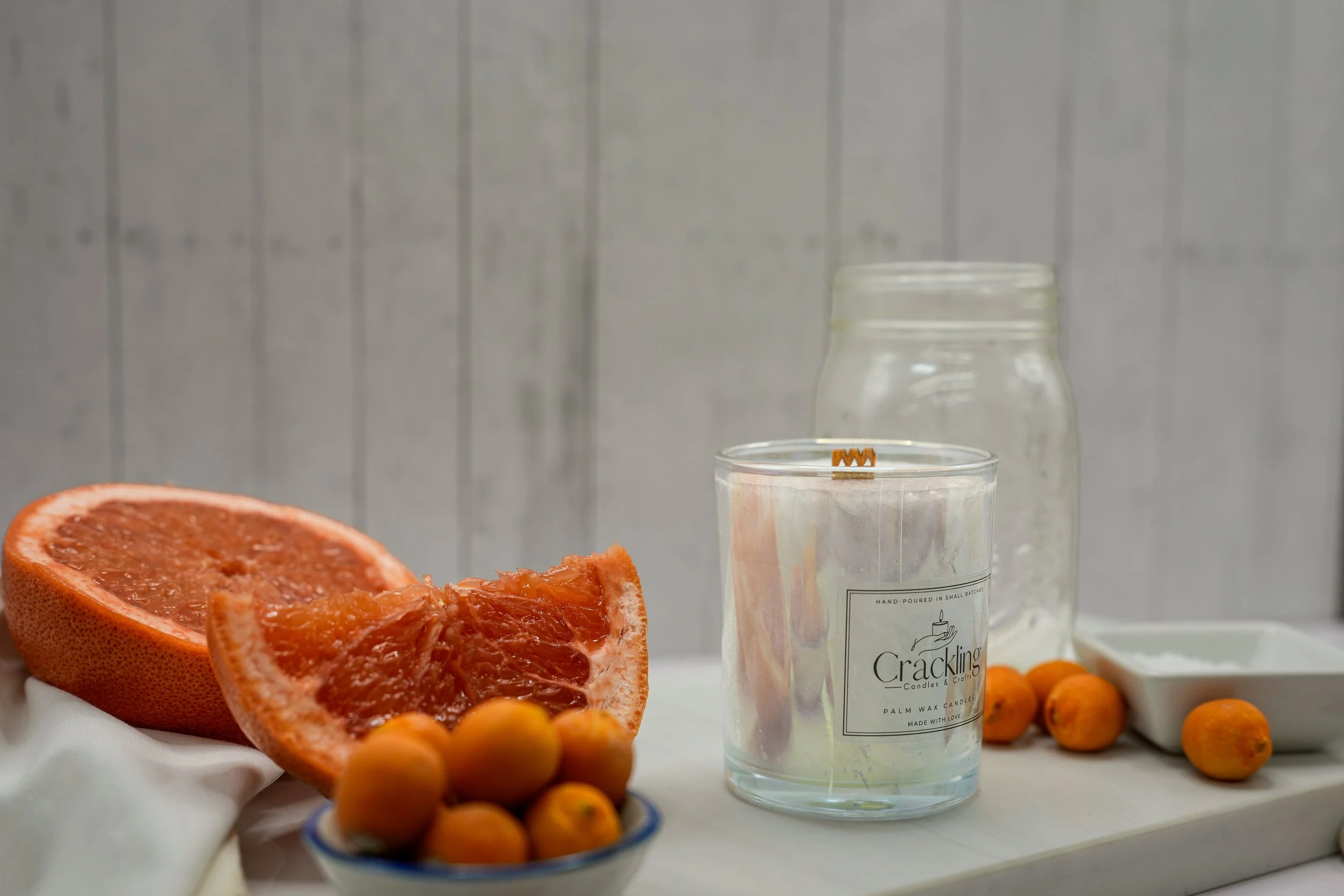 Grapefruit & Kumquat candle in a glass jar beside a cut grapefruit and fresh kumquats.
