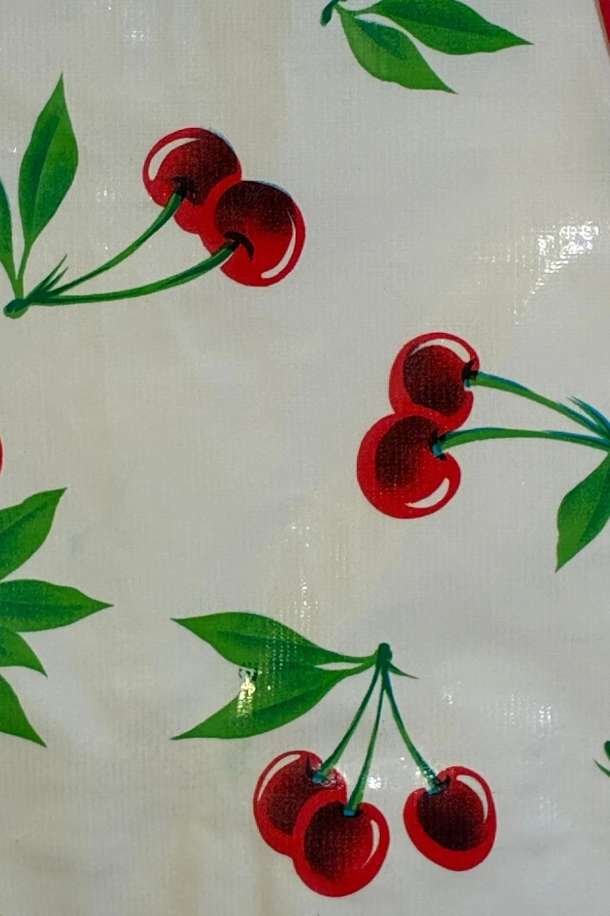 Close-up of the easy-clean oilcloth material with red cherries and green leaves on a light background.
