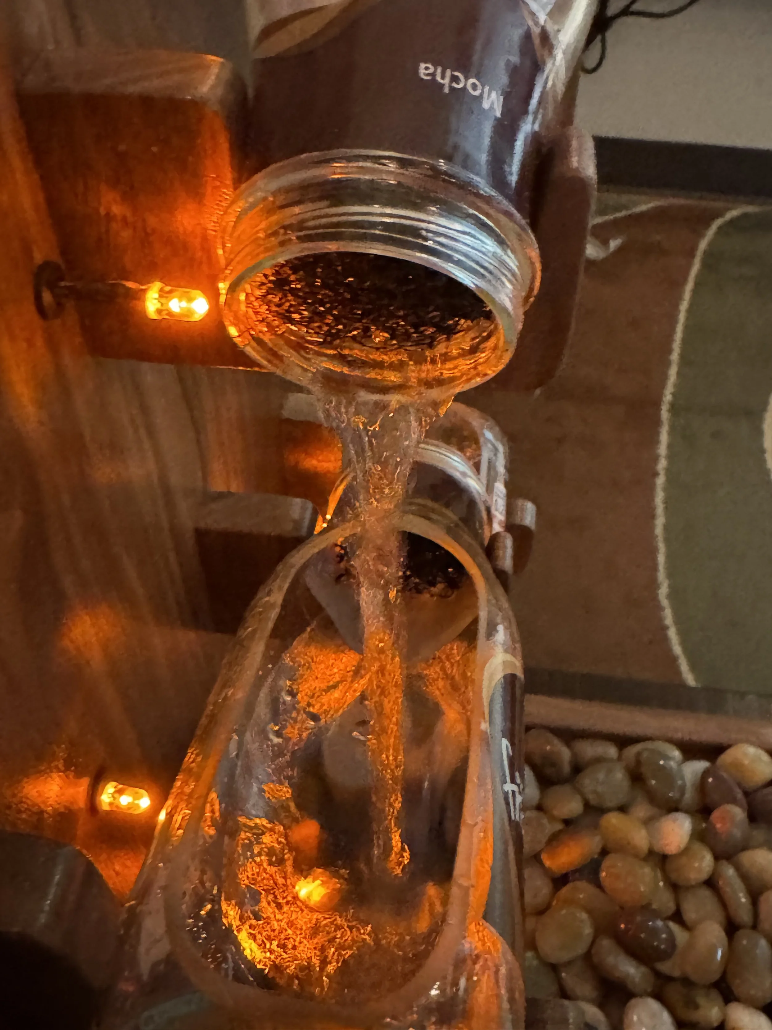 Close-up of water pouring from one Frappuccino bottle into another, illuminated by orange LED lights.