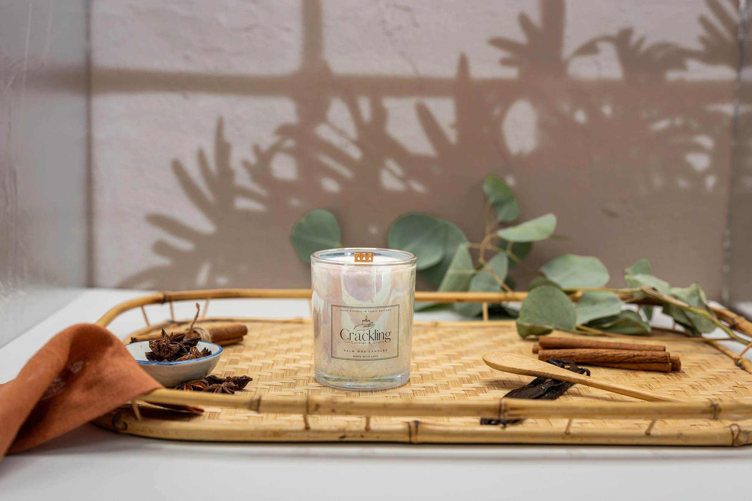 Hand-poured Cinnamon candle displayed with eucalyptus leaves, cinnamon sticks, and warm natural wood accents.