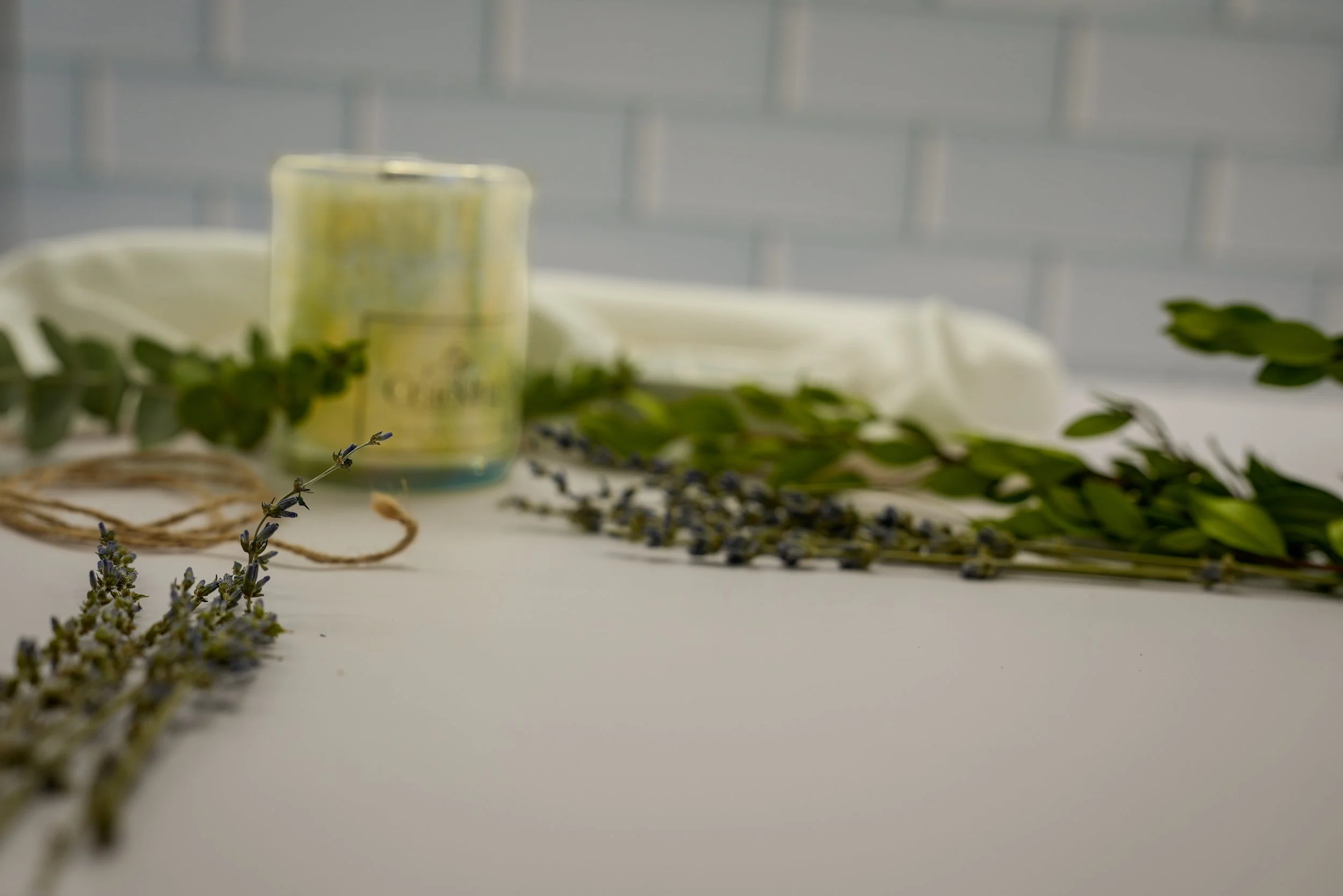 Honeysuckle palm wax candle styled with greenery and white fabric against a pale tile background