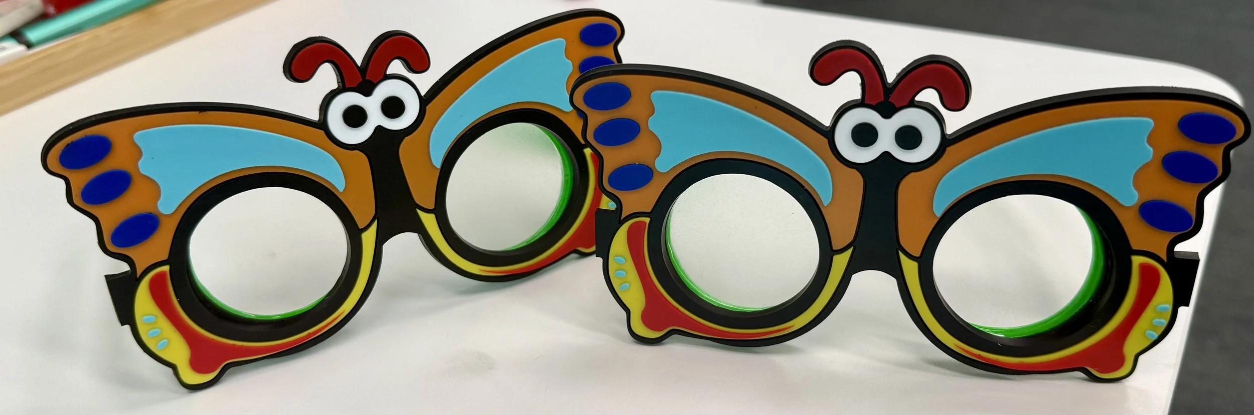 Two colorful butterfly-shaped novelty glasses with large circular lenses placed on a white surface.