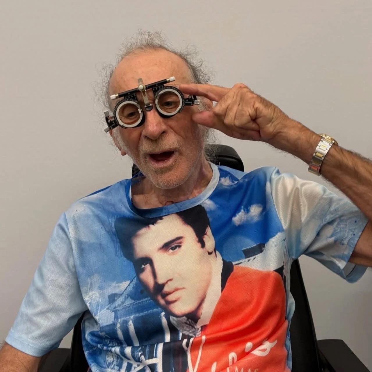 Image of a man wearing optometrist's 'trial frame' glasses.  He is wearing a t-shirt with Elvis on it and smiling.