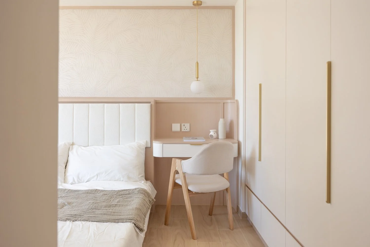 View through a doorway into a small room with a white chair, a desk, a hanging light, and a window with a plant on the sill, in a minimalist, modern interior.