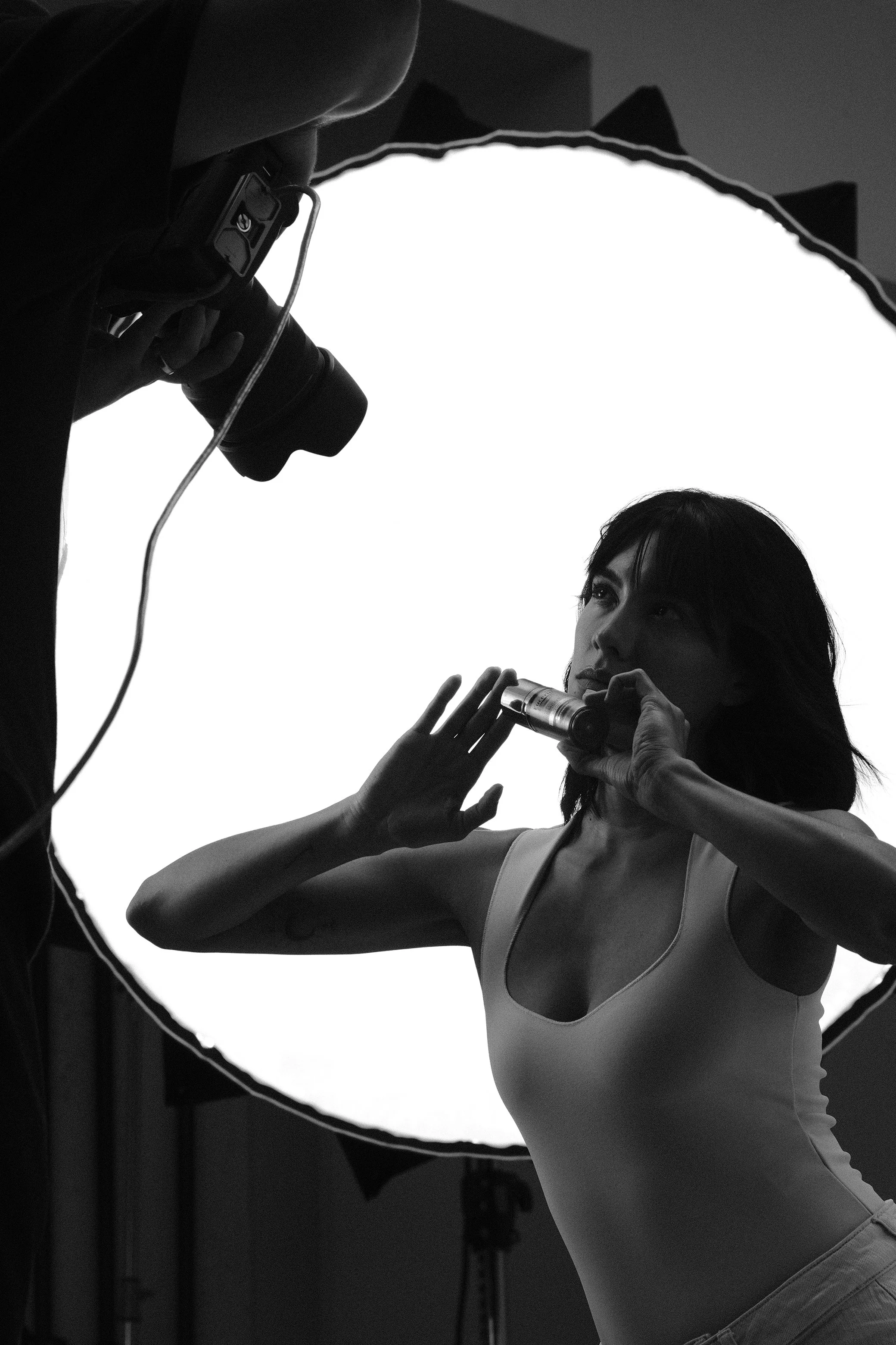 Schwarz-Weiß-Foto eines Fotoshootings: Eine Frau posiert vor einer hell erleuchteten Lichtquelle, während ein Fotograf mit Kamera die Aufnahme macht.