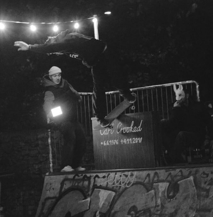 Ein Skateboarder macht einen Trick beim Überkopfsprung bei einer nächtlichen Skate-Veranstaltung, während eine Person mit Hasenmaske zusieht.