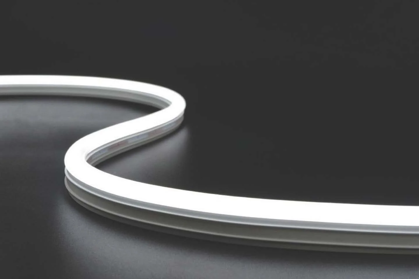 A close-up of a wavy, white LED light strip on a dark surface.