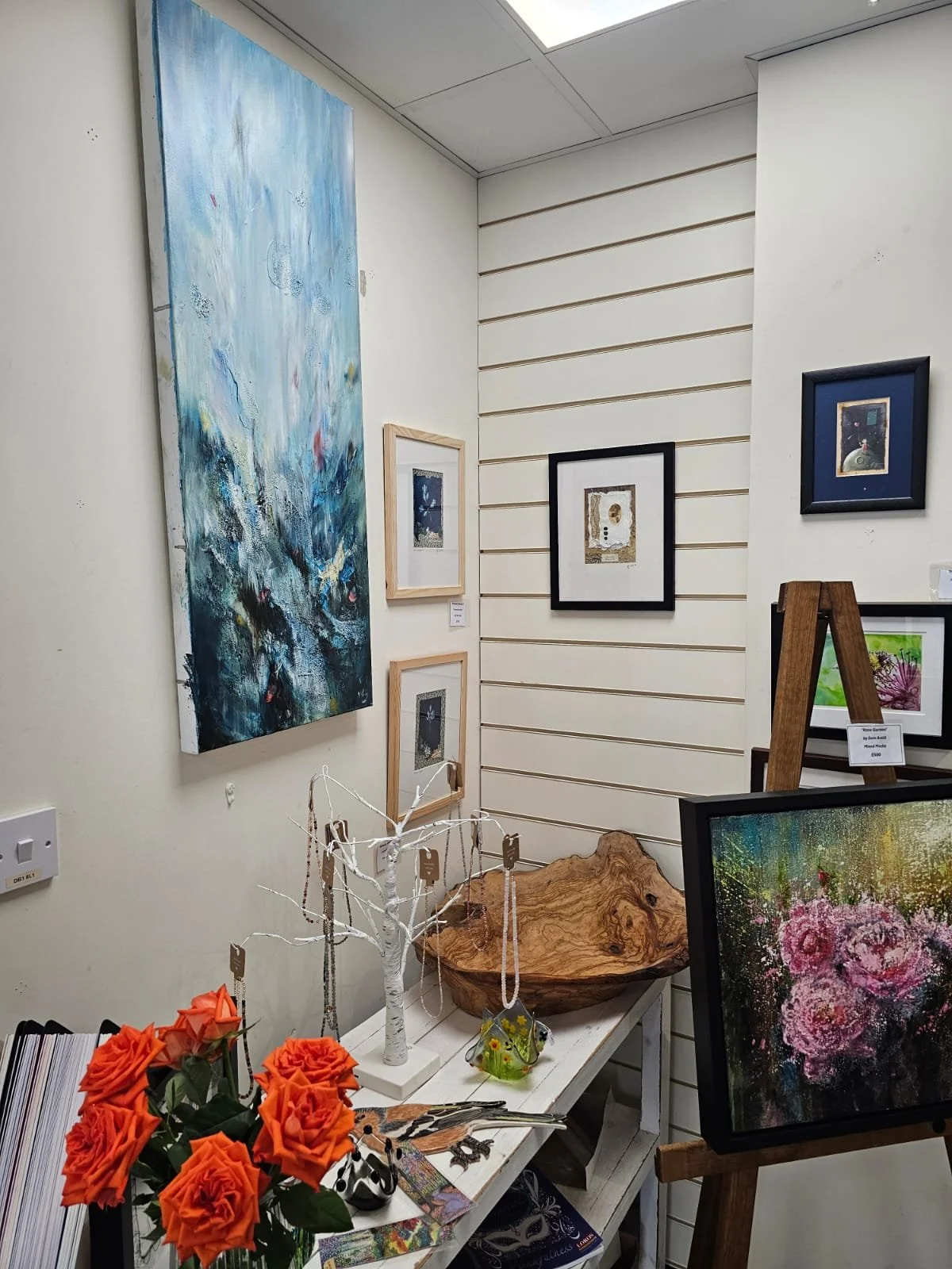 Interior of an art gallery with paintings on the walls, a table with decorative items and framed artwork on display