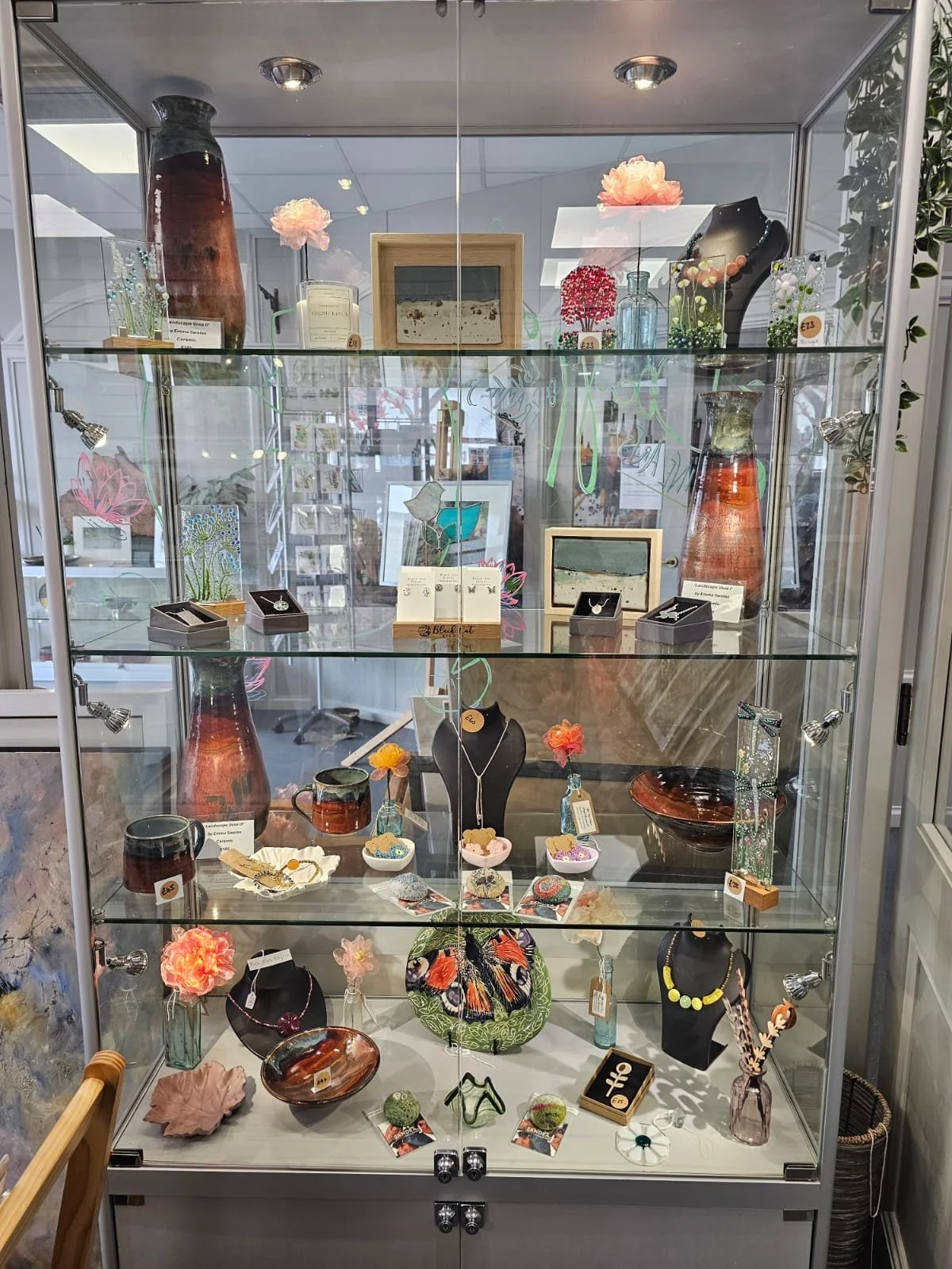 A glass display case showcasing various handmade jewelry, decorative ceramics, artwork, and small decorative items.