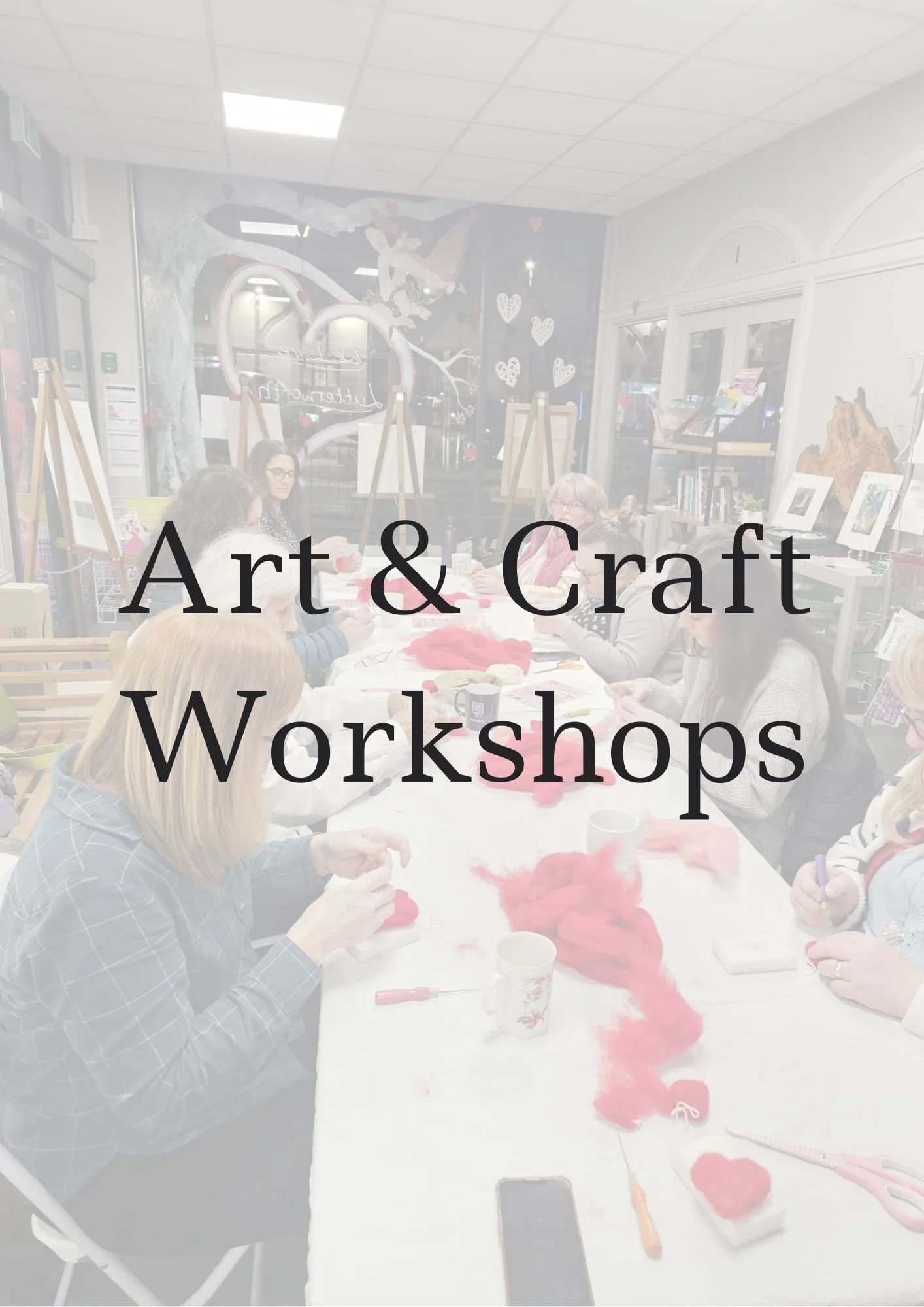 People participating in a craft workshop at a long table with red yarn, scissors, and craft supplies inside a store with art displays and a painted wall.