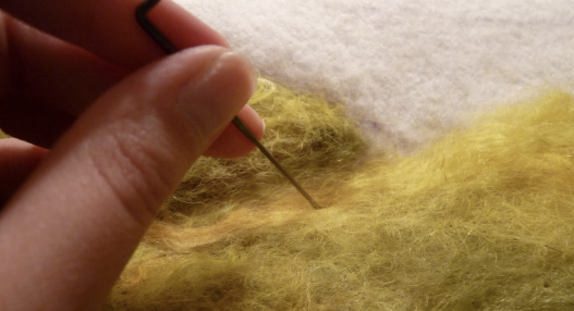 Close-up of a hand using a felting needle to felt yellow felt fabric.