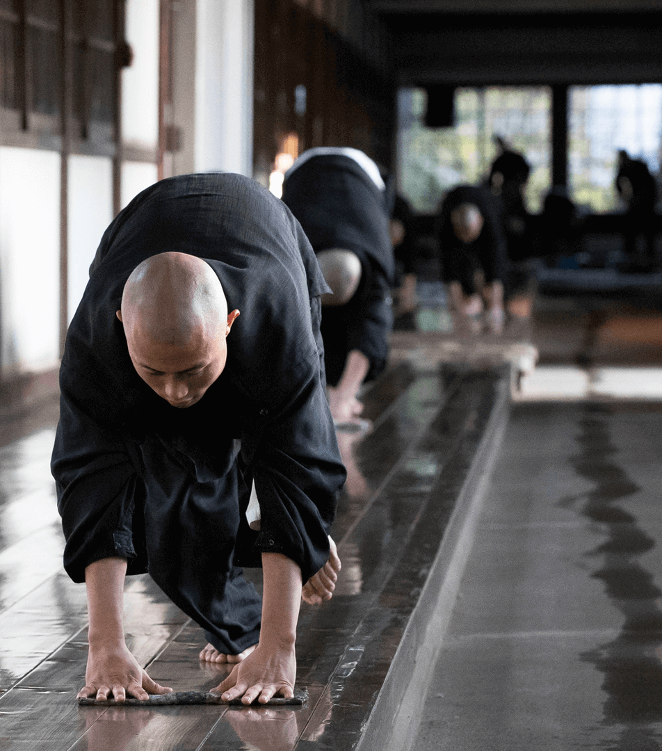 Practican budismo en un templo japonés, realizando la ceremonia del agua con ropas tradicionales y barriles de agua a su lado.
