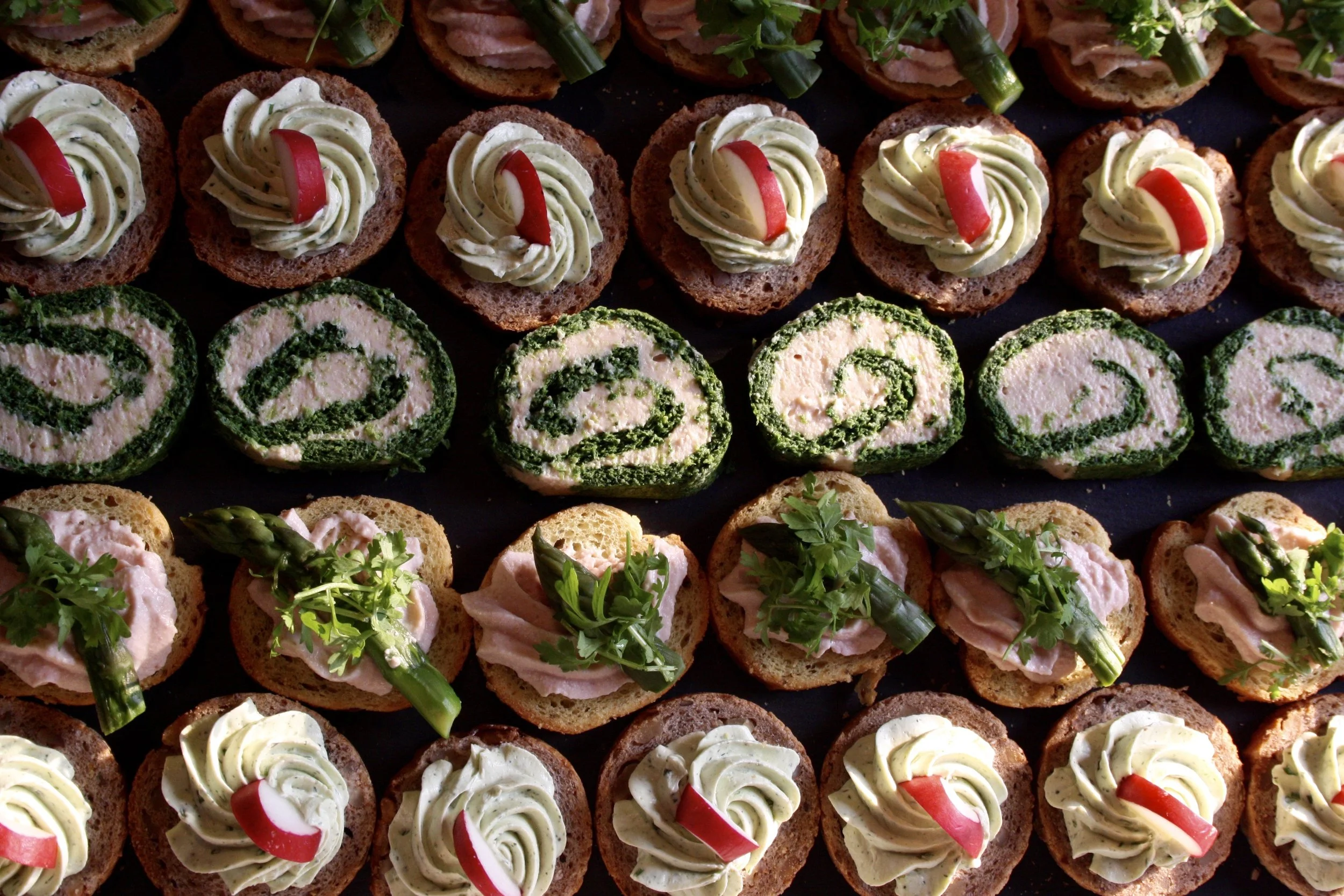 Assorted canapés with various toppings including cream cheese, smoked fish, red peppers, and herbs on bread or crackers, garnished with parsley and asparagus.