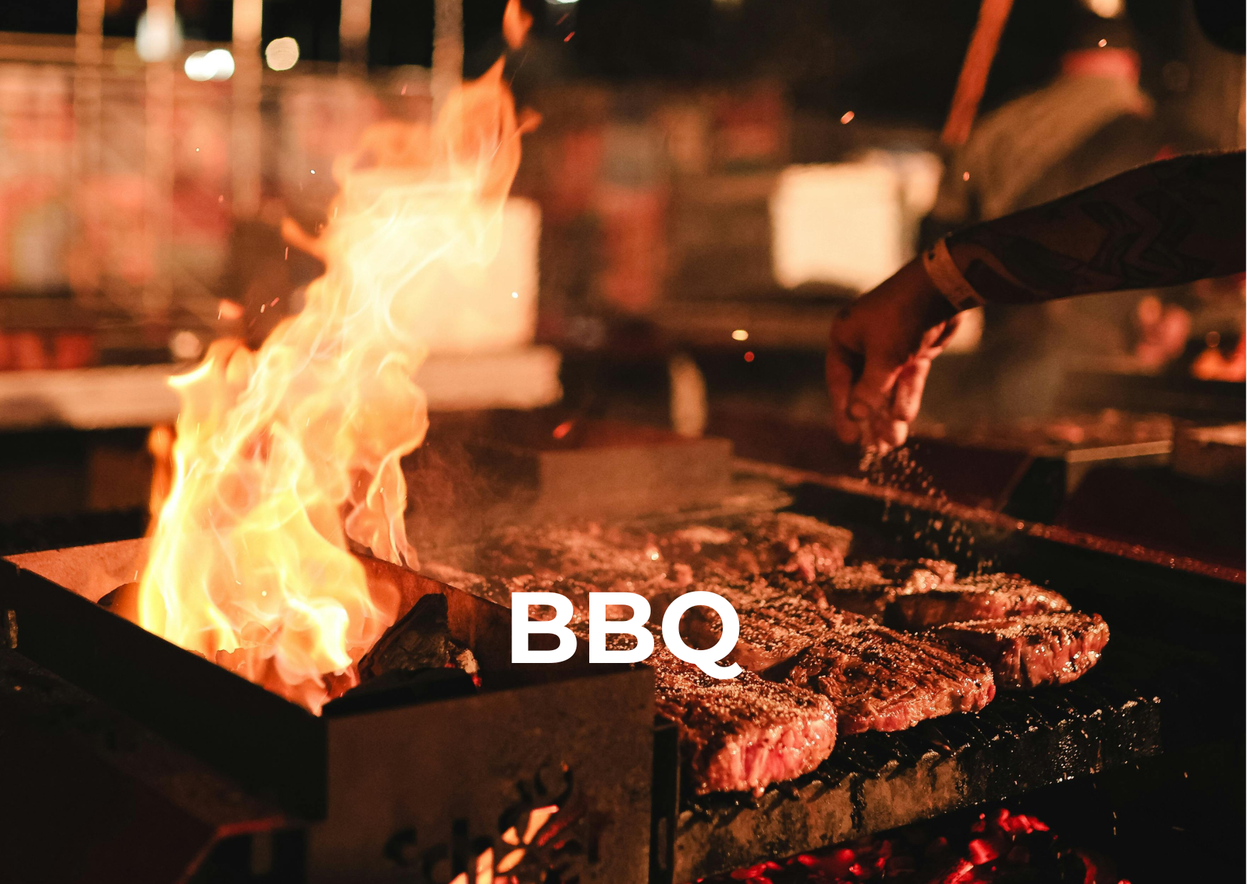Close-up of steaks cooking on a grill with flames. A person's hand is seasoning the meat while other grill marks are visible. The word 'BBQ' is written in white text at the bottom.