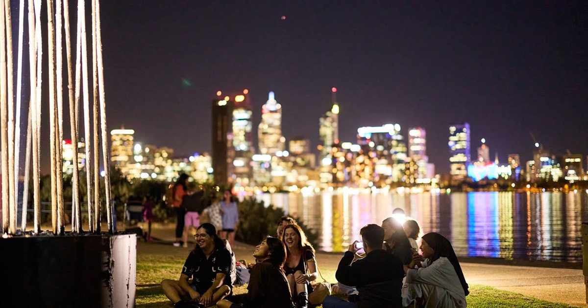 A group gathered beside illuminated poles overlooking the city at night.