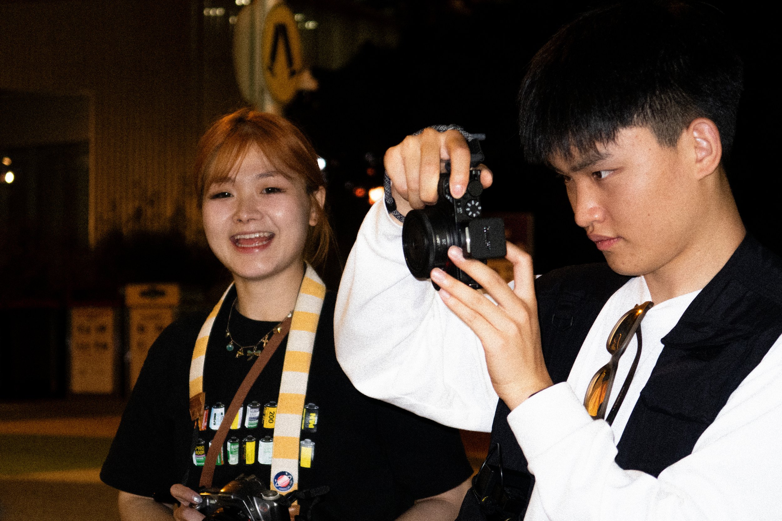 Two photographers at night, one smiling while the other reviews a camera.