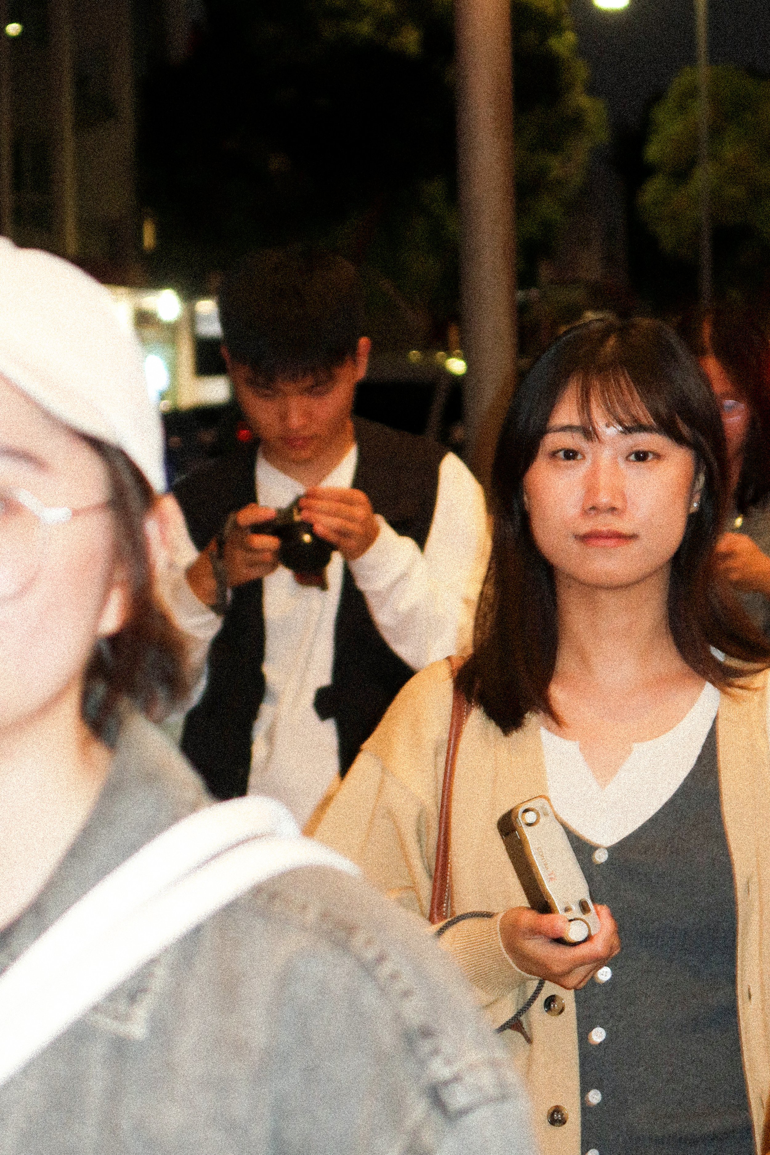 Young woman holding a film camera at night, with other photographers in the background.