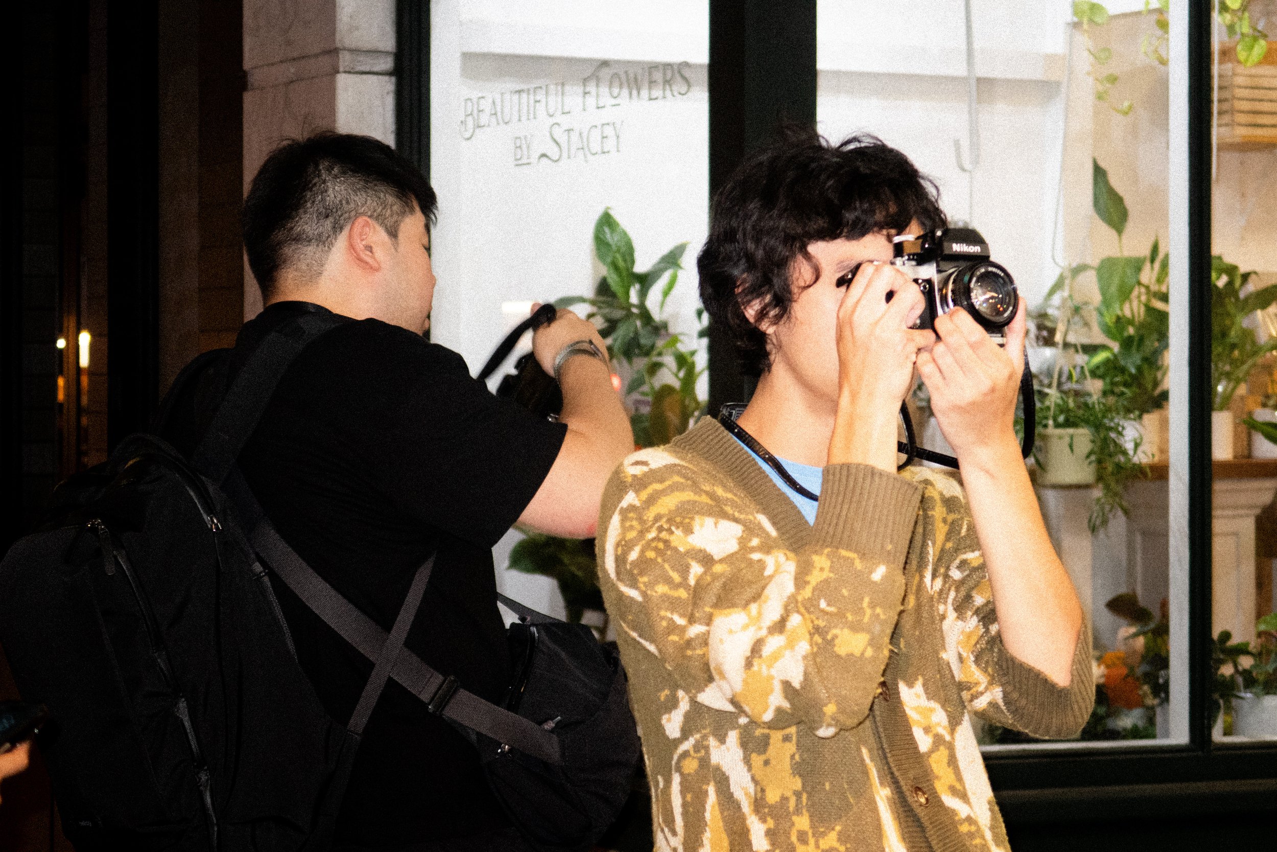Two photographers at night, one taking a photo while another adjusts their camera bag.