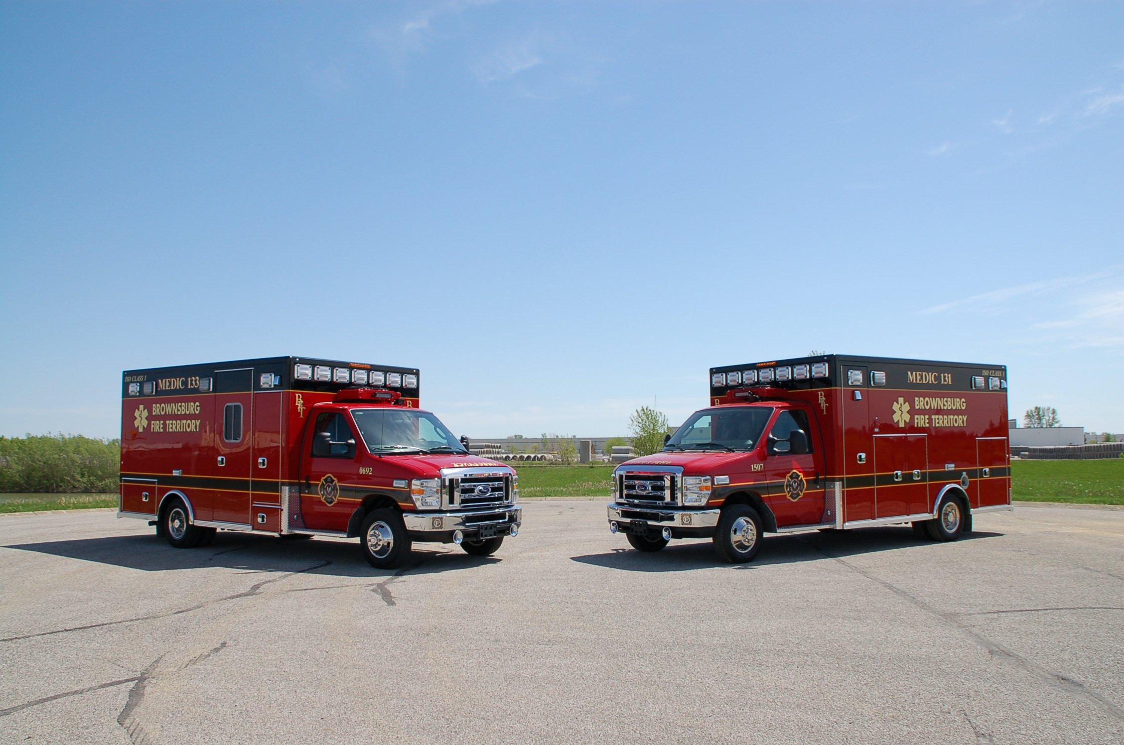 Two red emergency vehicles labeled Browensburg Fire Territory parked on a paved lot under a clear blue sky.