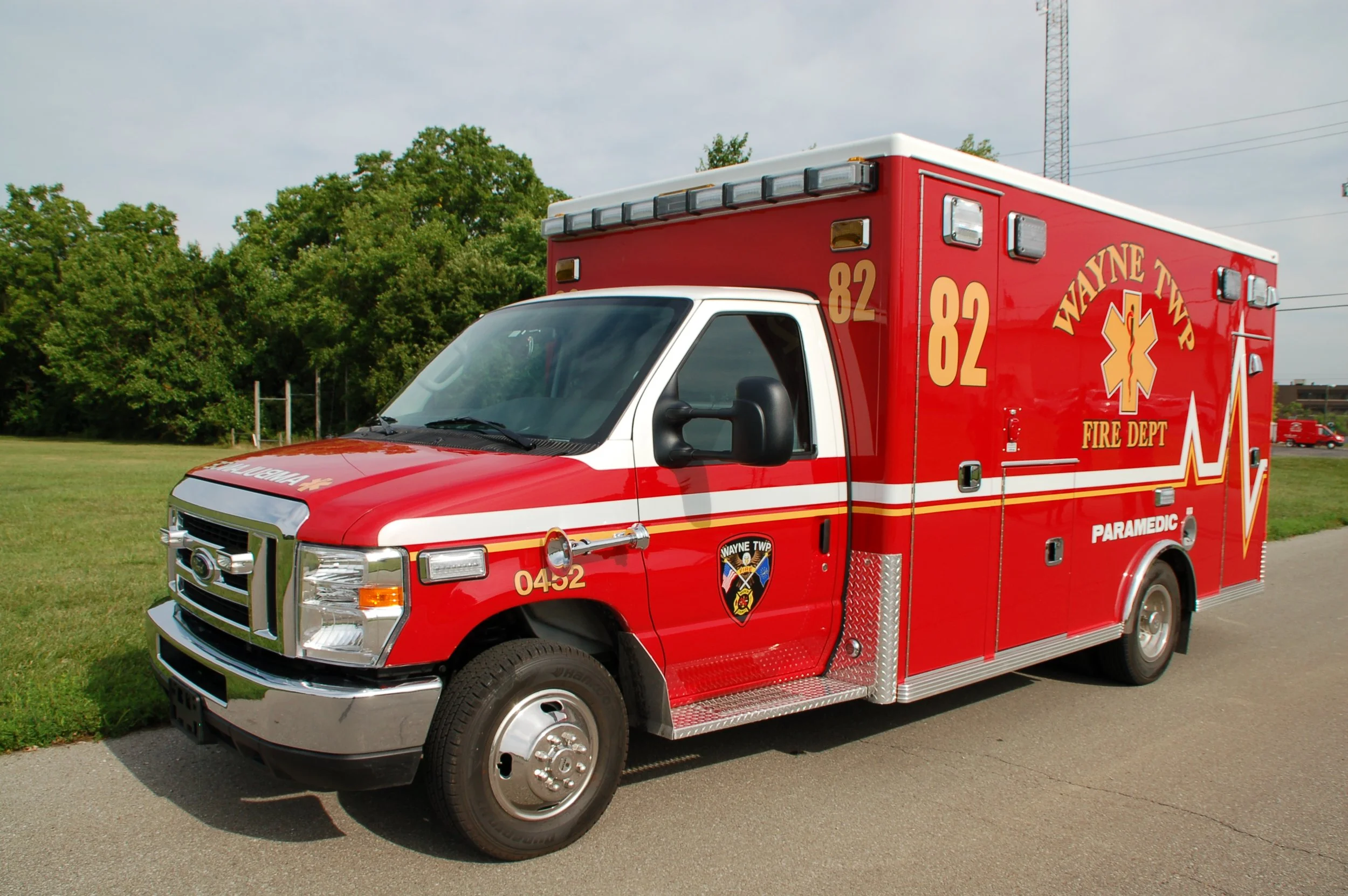 Red Wayne Township Fire Department ambulance parked on a paved area next to a grassy field with trees in the background.