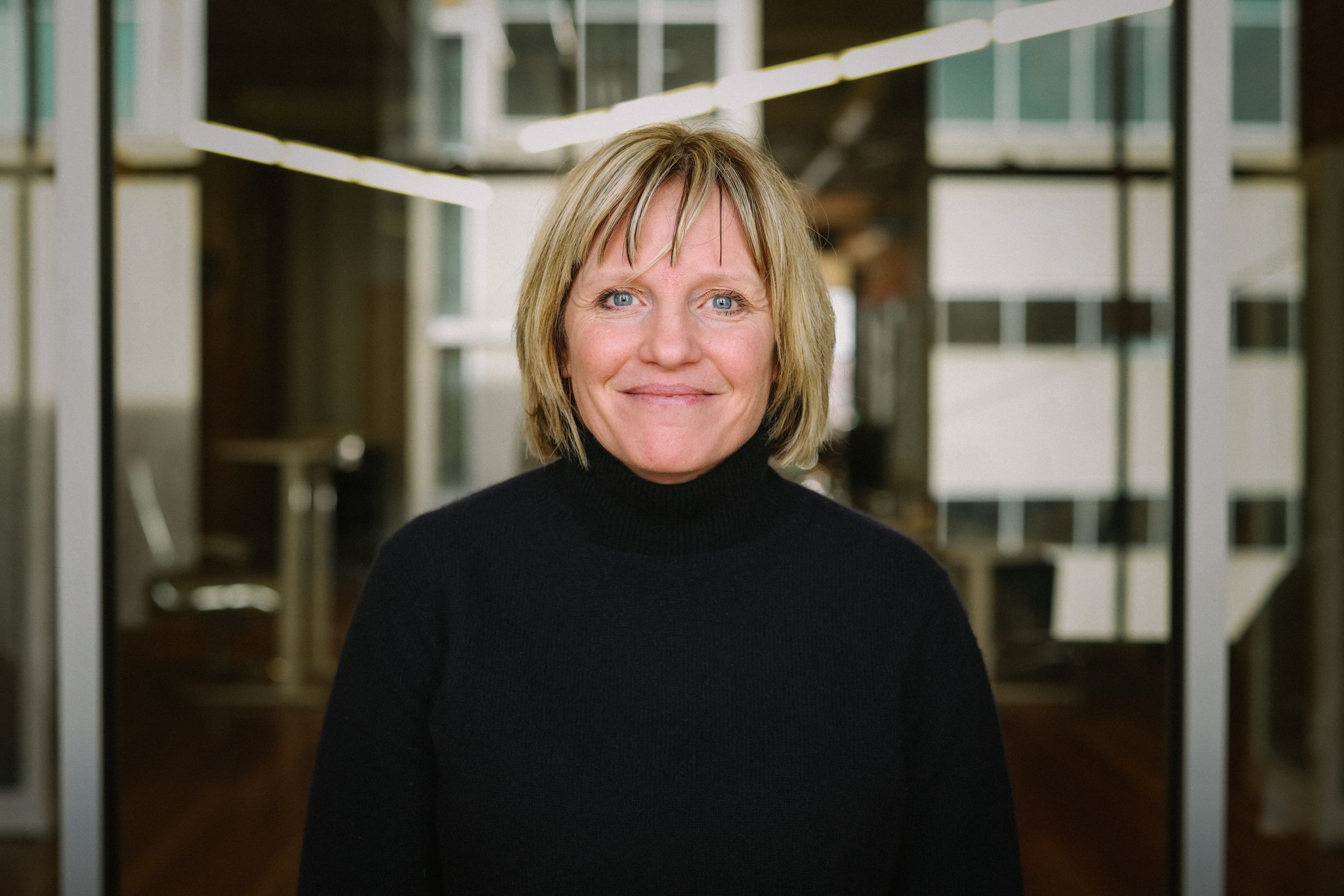 Ingrid Wadell in an office conference room with glass reflecting a downtown scene behind her.